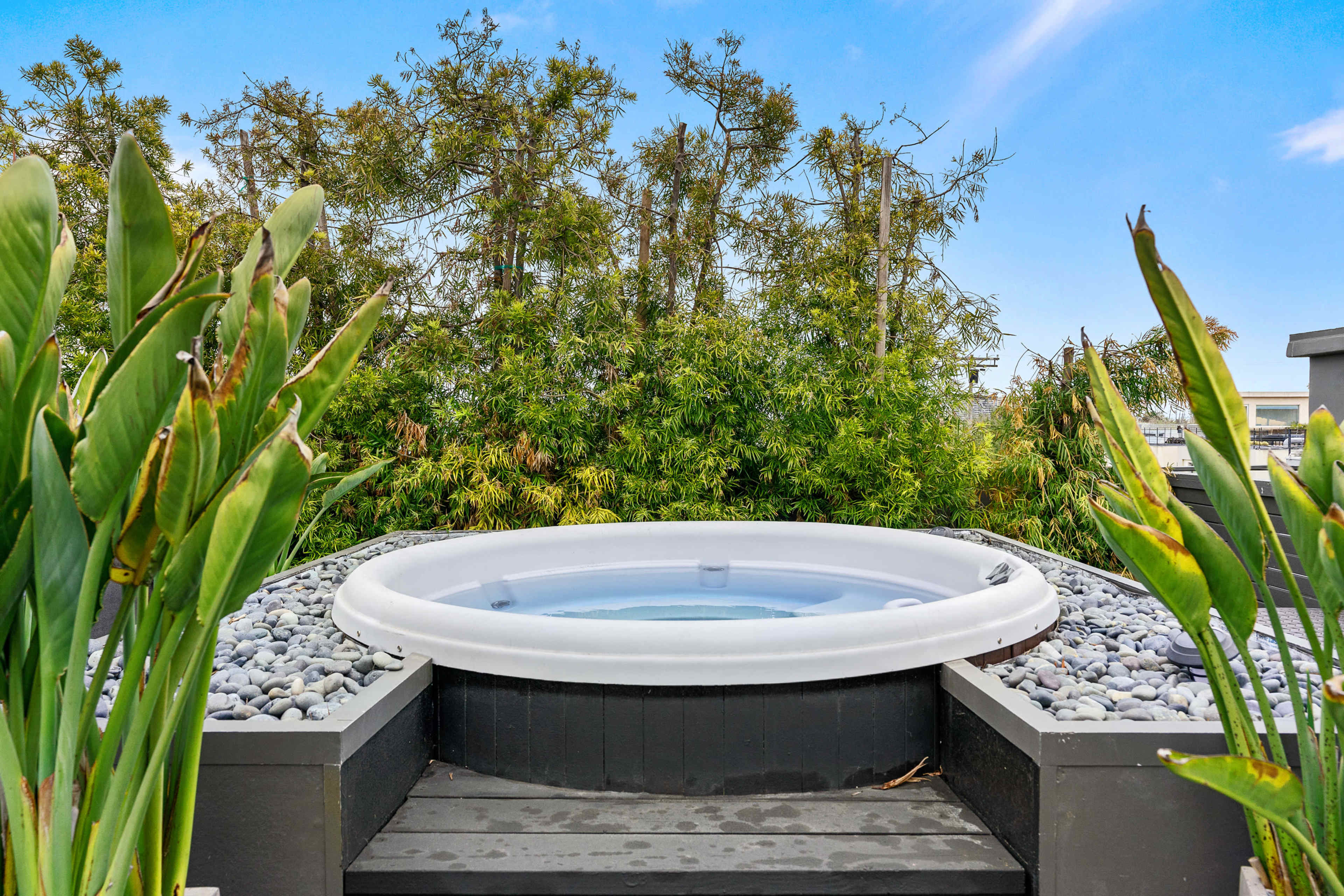 A round hot tub surrounded by smooth stones and greenery is prominently featured in the image.