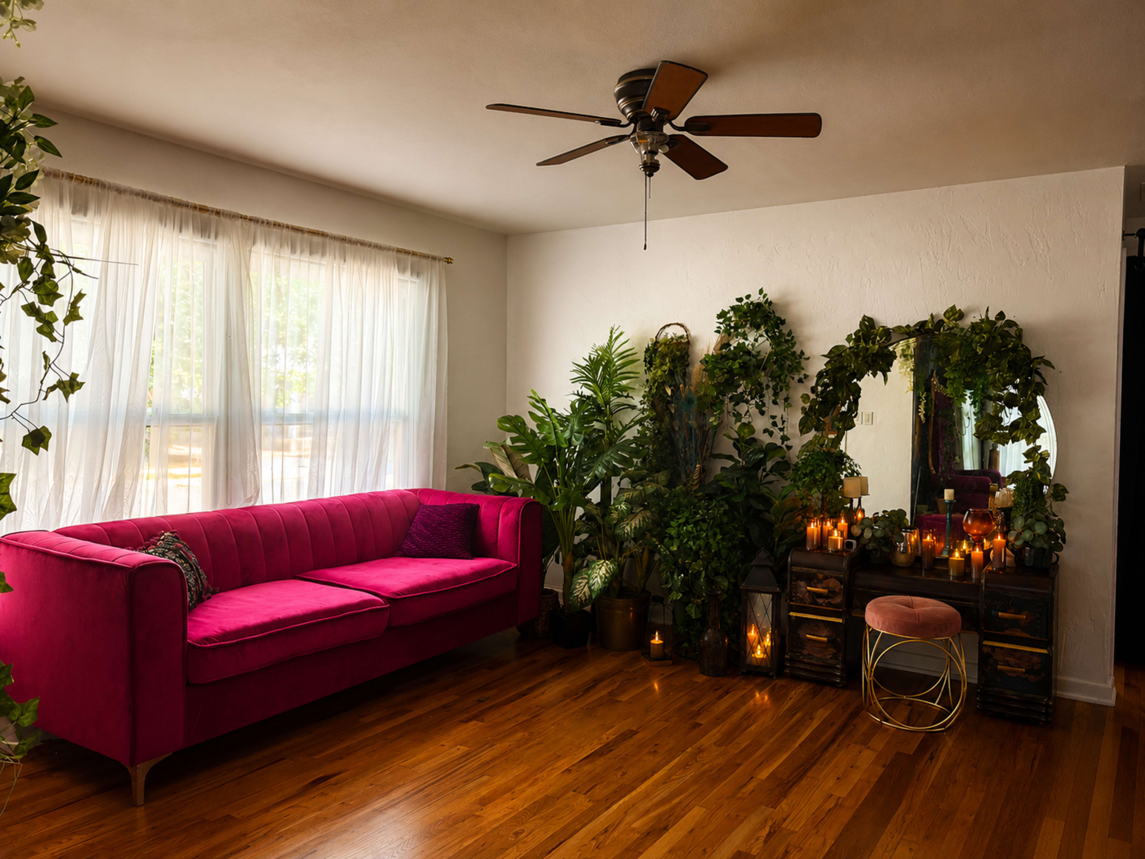 The image shows a bright living room featuring a pink sofa, a mirror with plants surrounding it, and several candles arranged on wooden furniture.