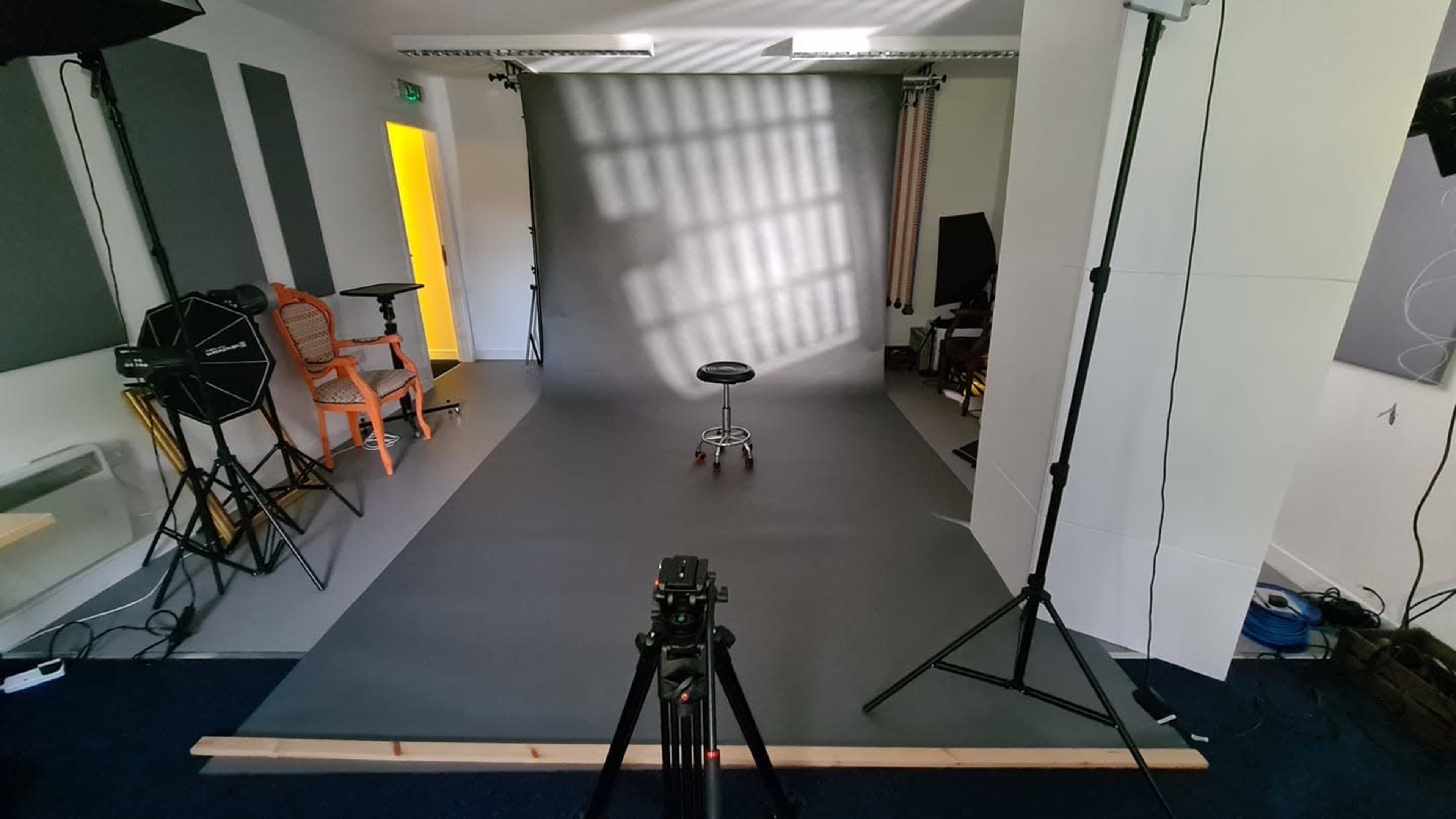 A photography studio features a gray backdrop, a stool in the center, and various lighting equipment set up around the space.