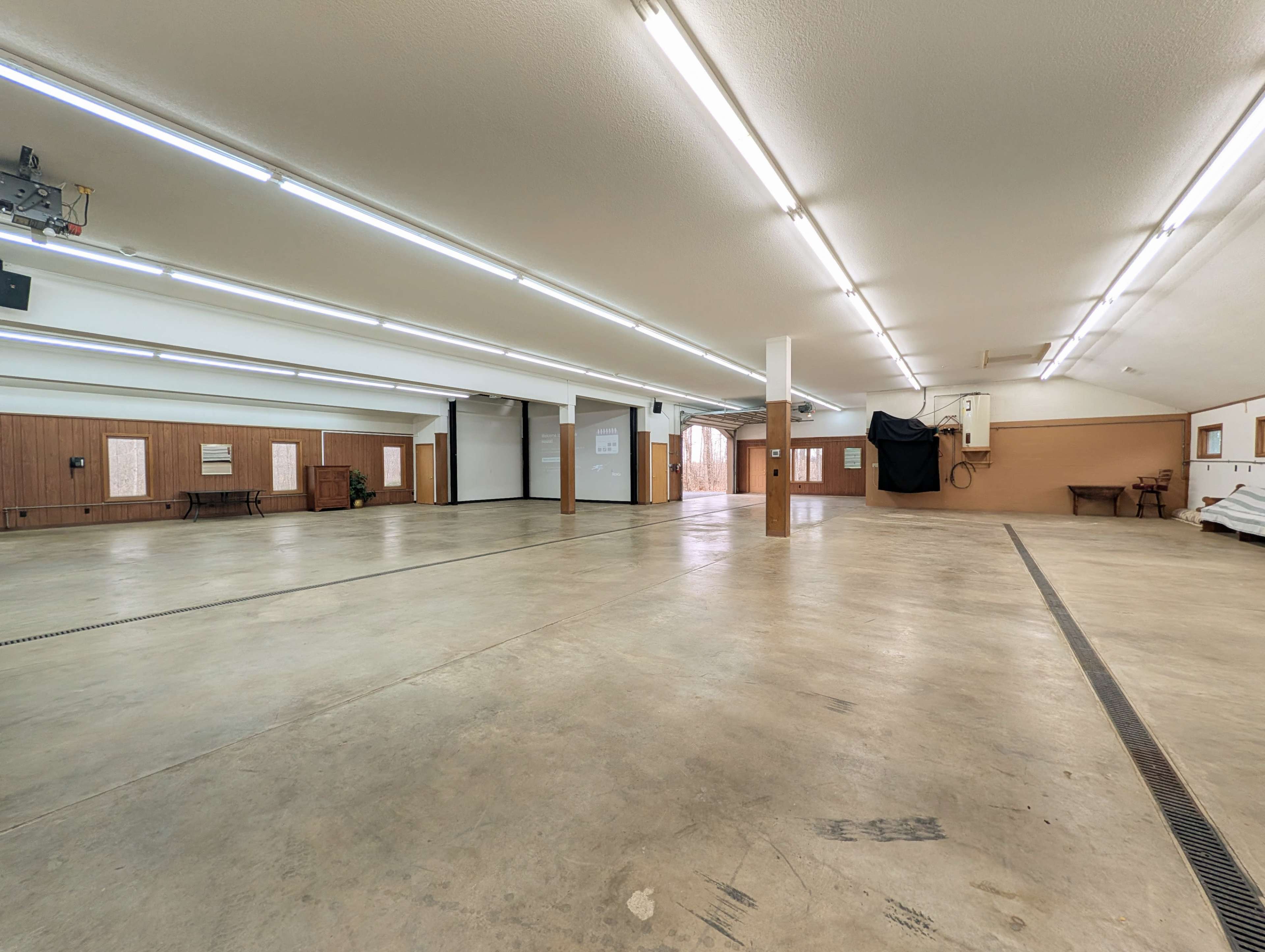 The image shows a spacious, well-lit interior area with concrete flooring and wooden paneling, featuring multiple entry points and a large, open floor plan.