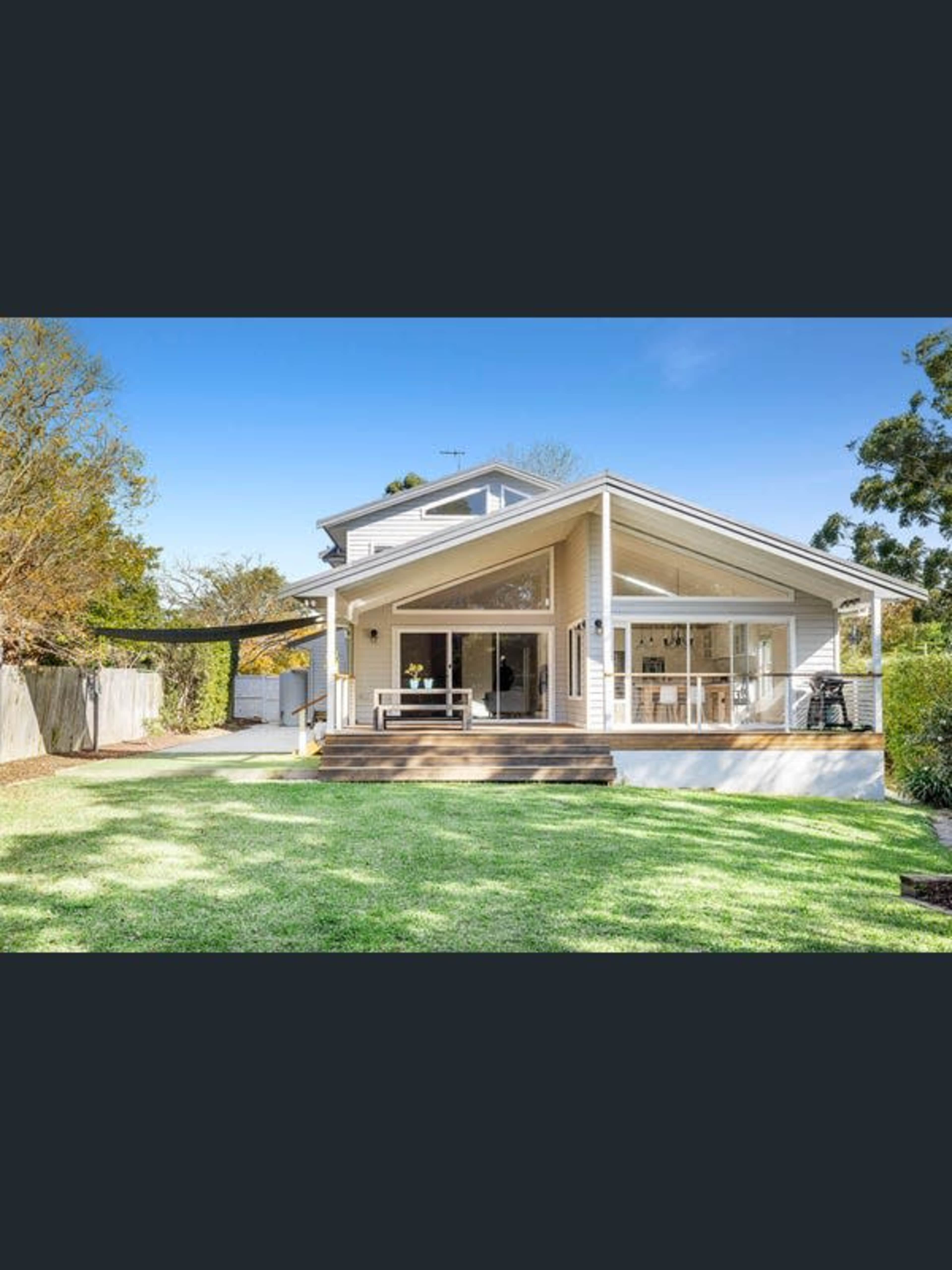 A modern two-story house with a large deck overlooks a neatly maintained lawn and garden.