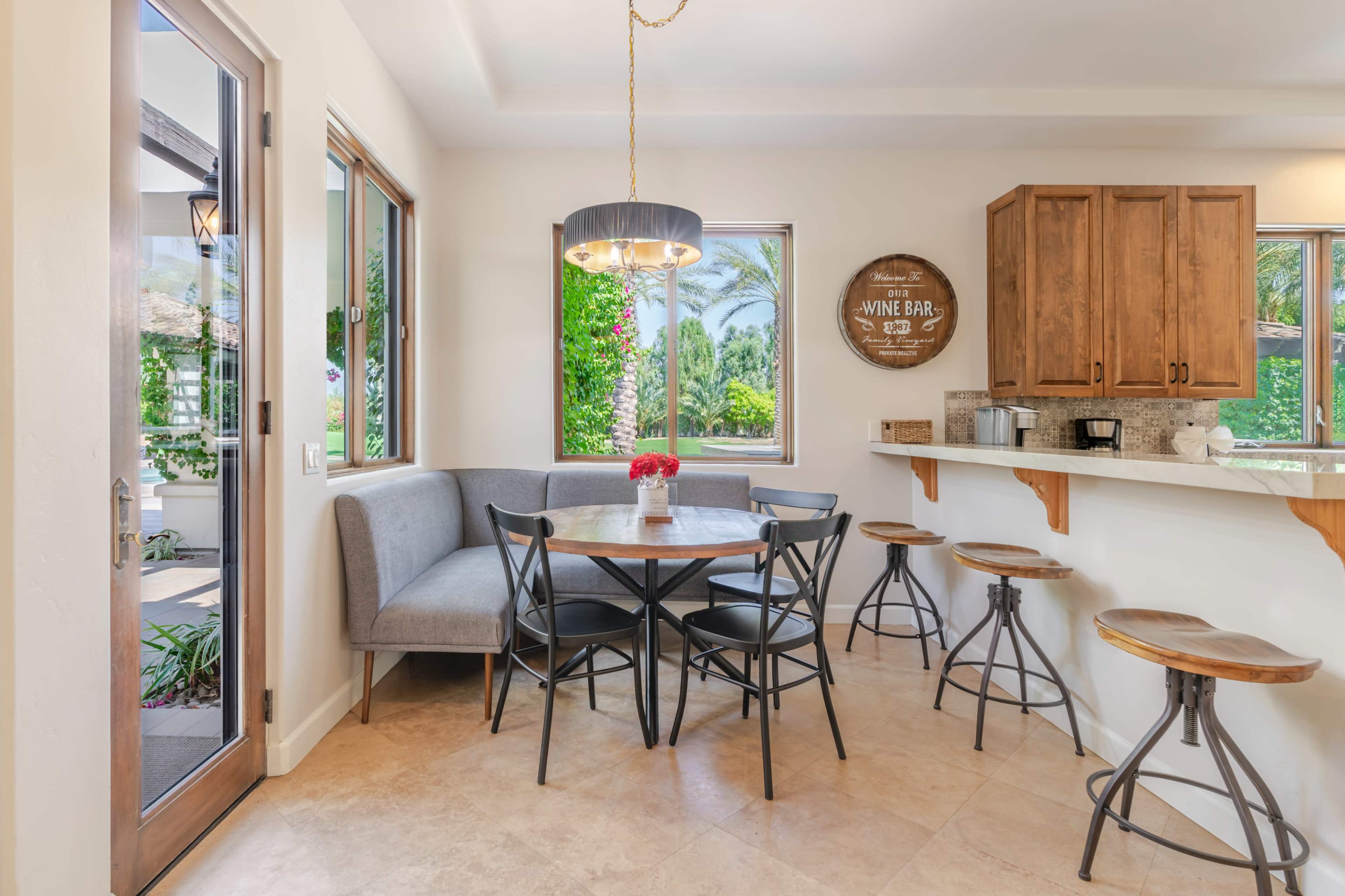 The image shows a small dining area with a round table surrounded by black chairs, a built-in bench, and wooden cabinets along the wall.