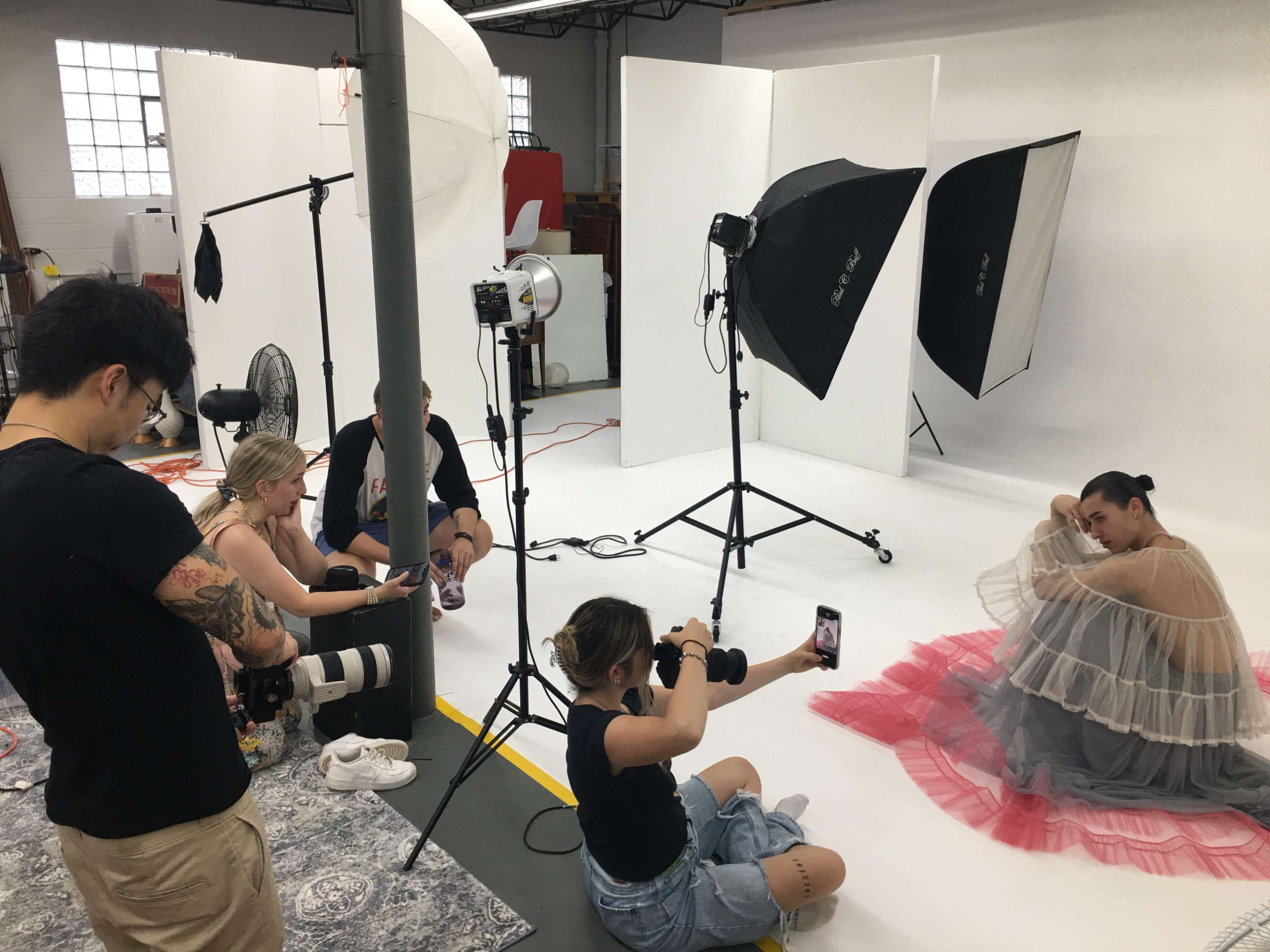 A group of photographers and assistants are setting up a photoshoot with a model in a studio, featuring backdrop lights and equipment.