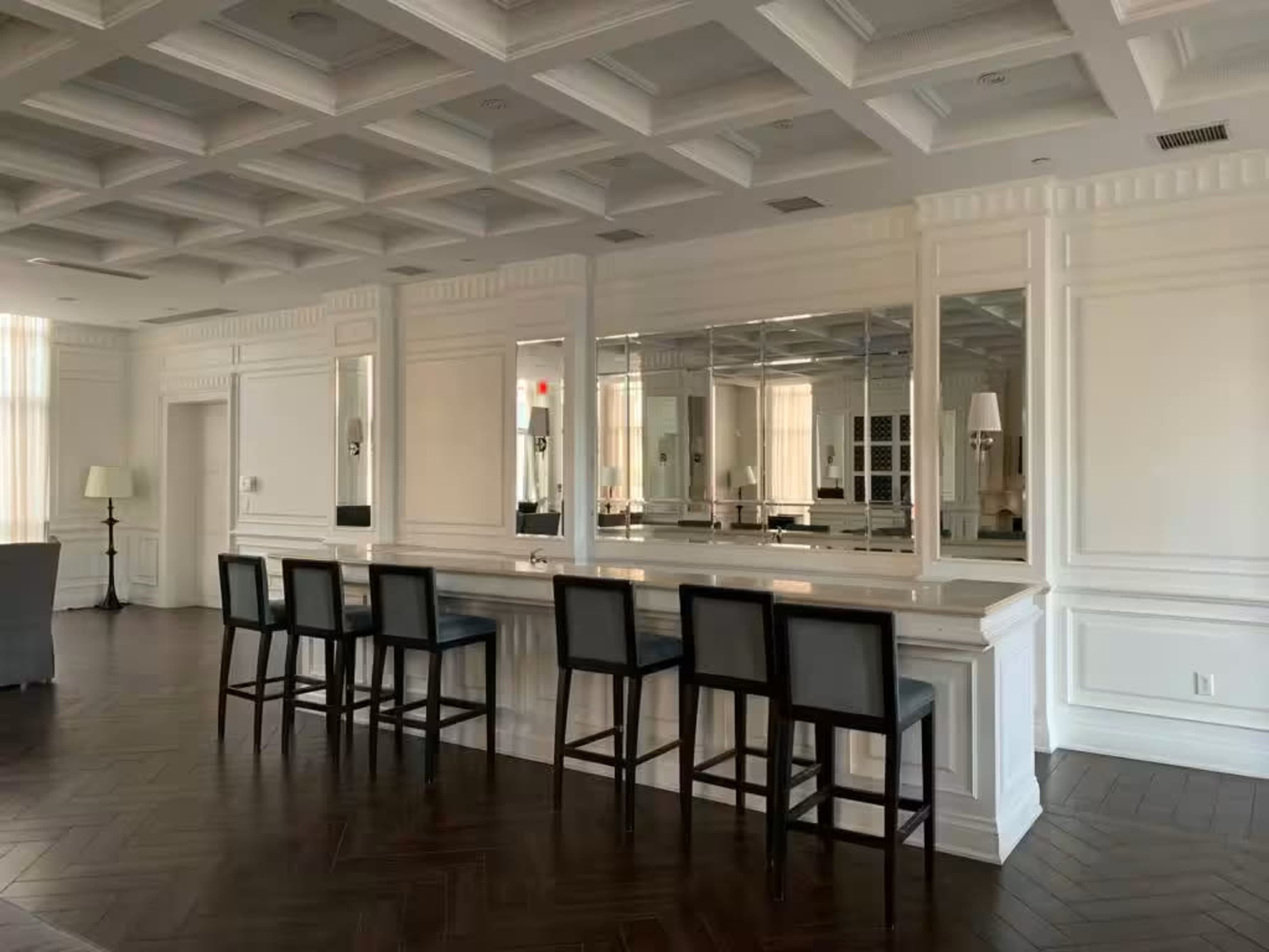 A spacious room with a long countertop and several tall bar stools facing a mirrored wall.