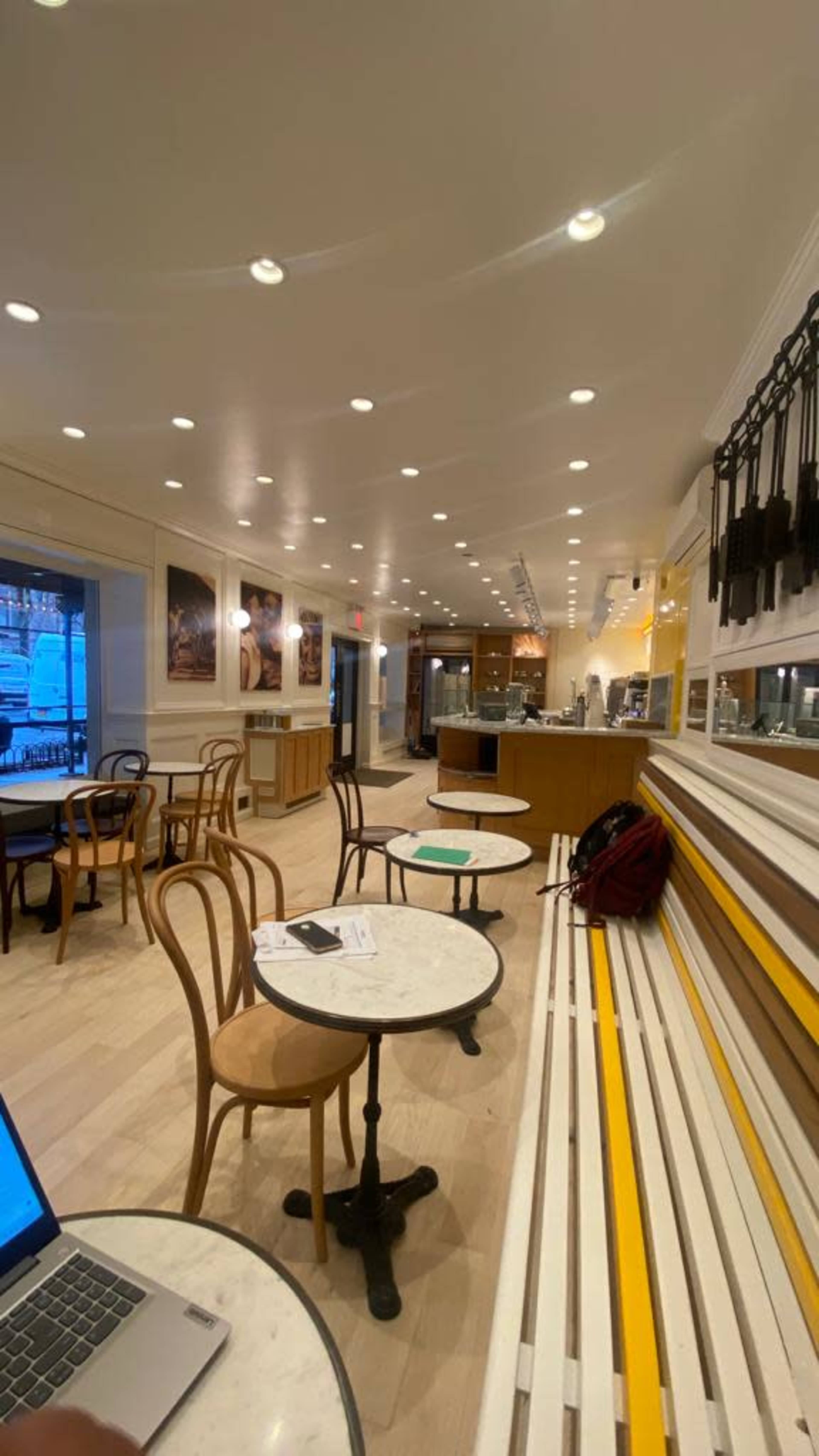 The image shows a cozy café interior with wooden chairs, round marble tables, and bright overhead lighting.