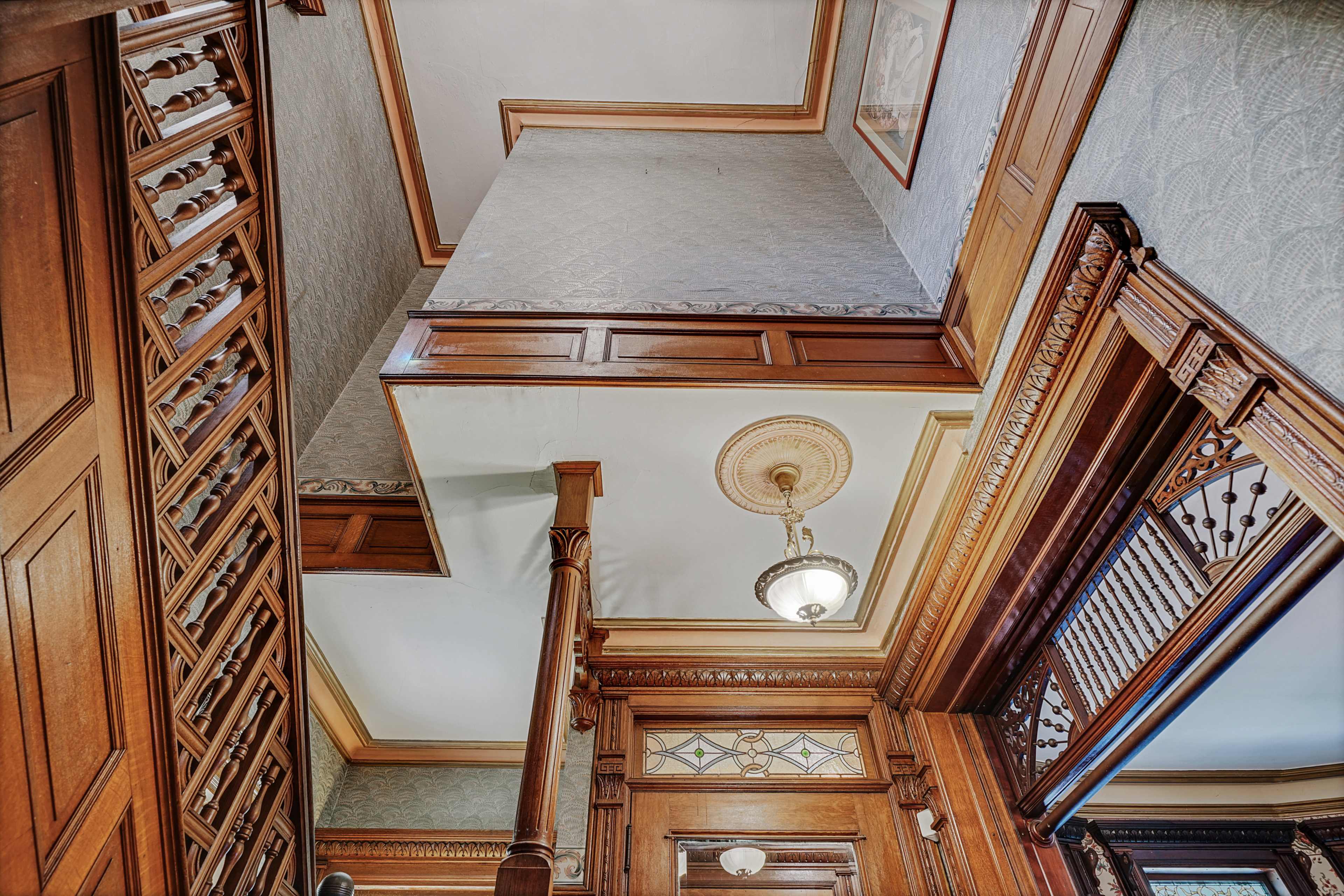 A staircase leading to a landing in a wooden interior with ornate molding and a decorative light fixture.