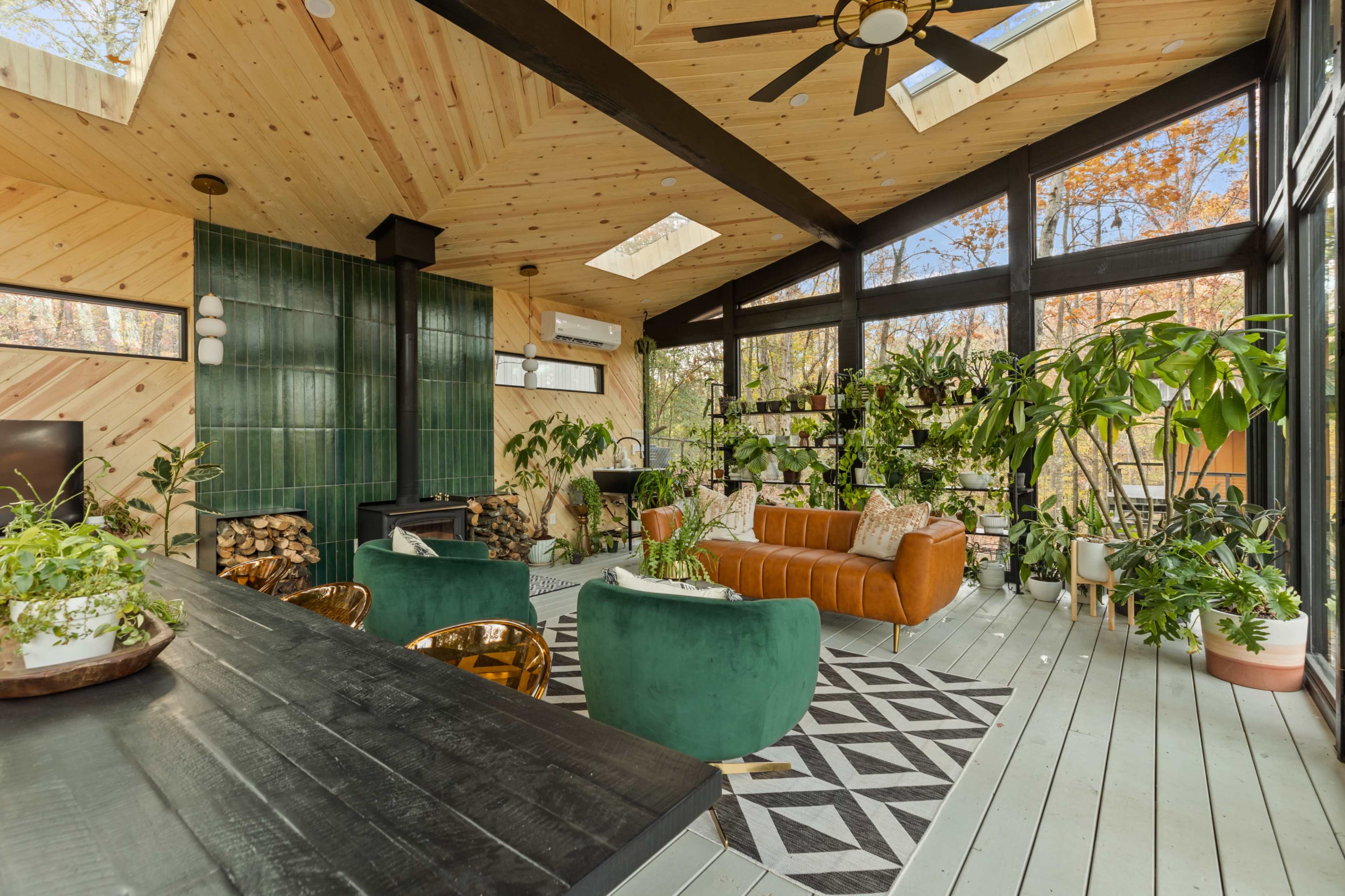 A modern living room features large windows, a combination of leather and velvet furniture, and numerous indoor plants.