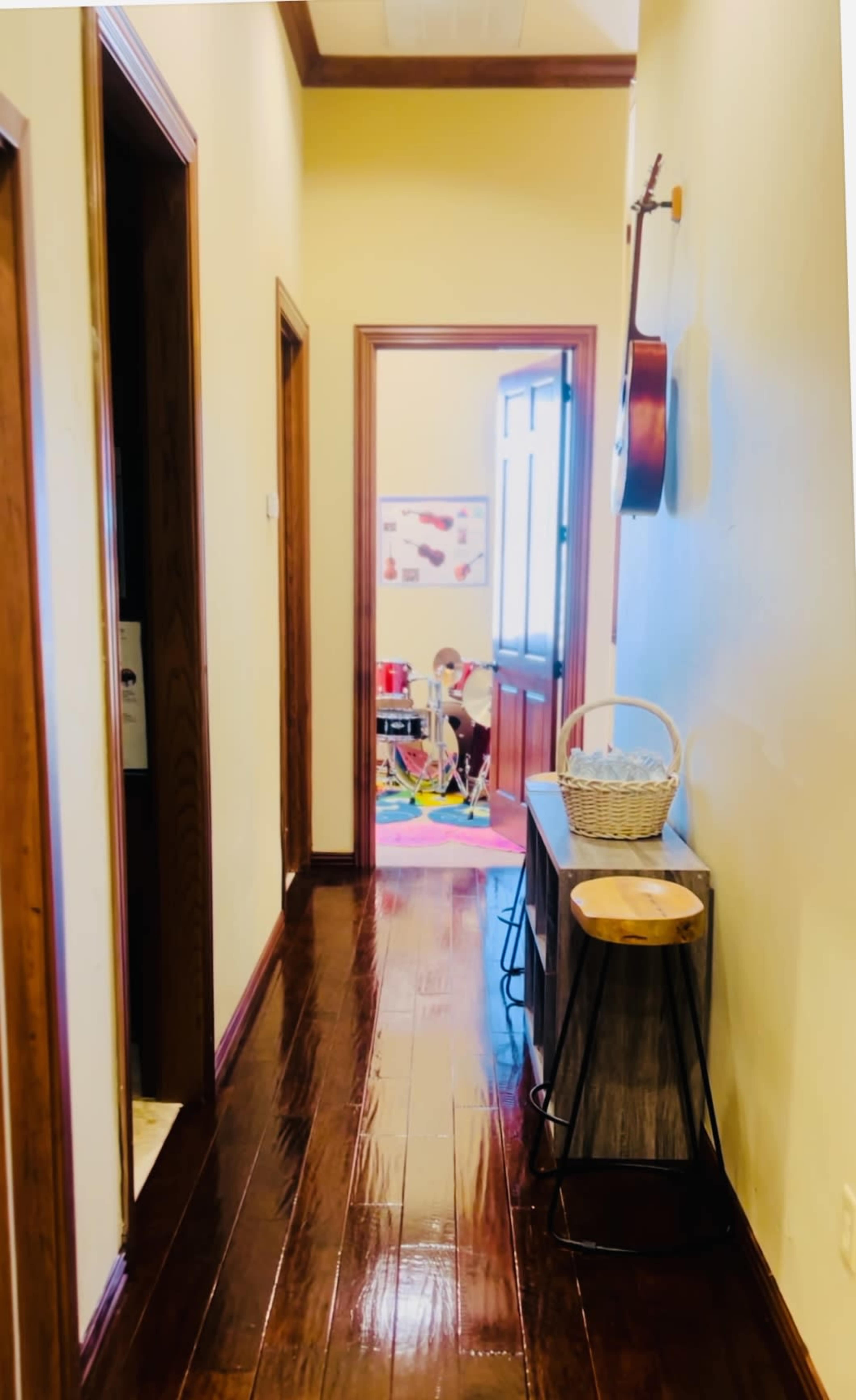 A hallway with wooden floors, two doorways on the left, and an open door at the end leading to a colorful room.