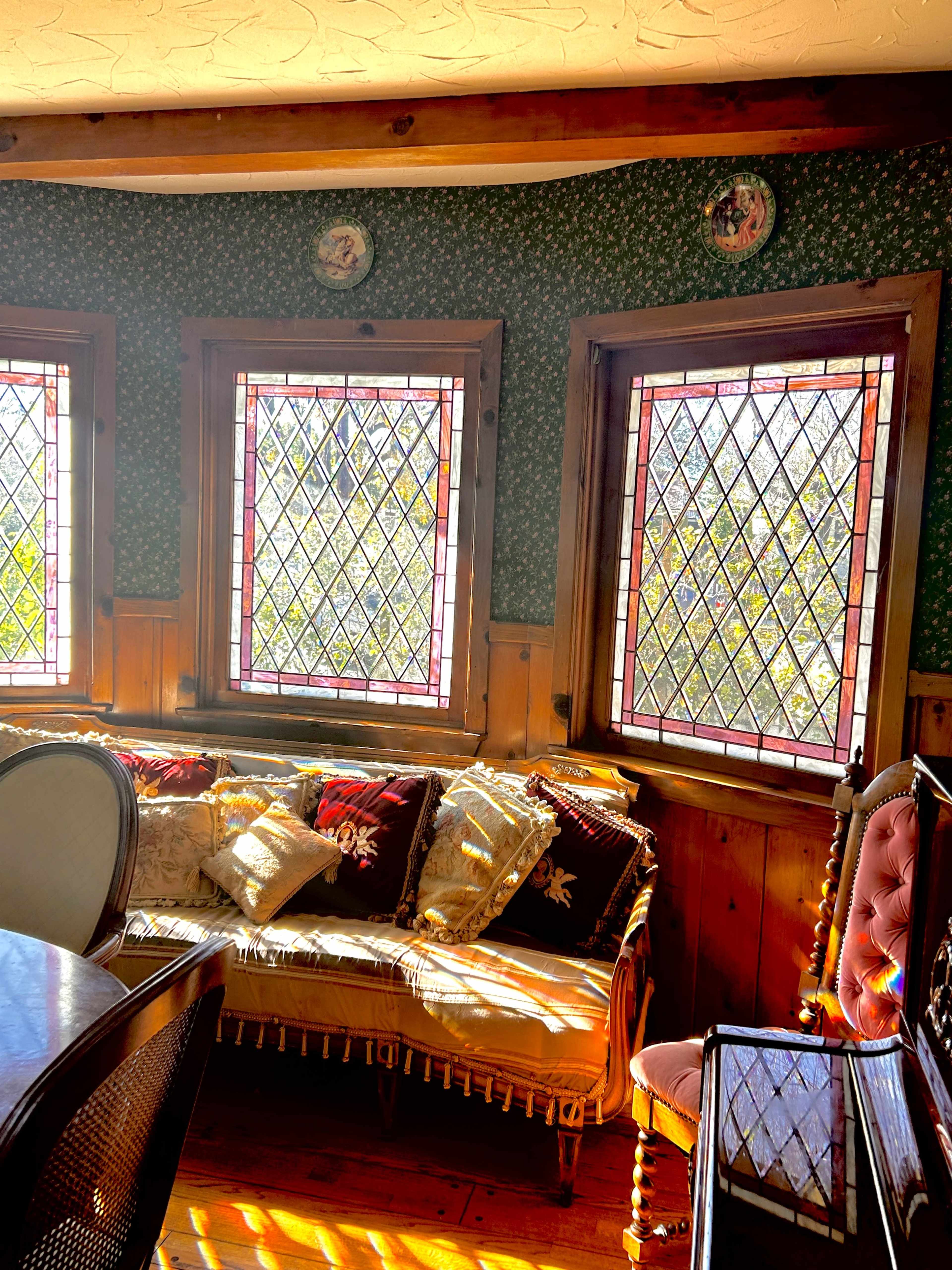 A cozy sitting area featuring a sofa with decorative cushions beside three diamond-patterned windows that allow natural light to stream in.
