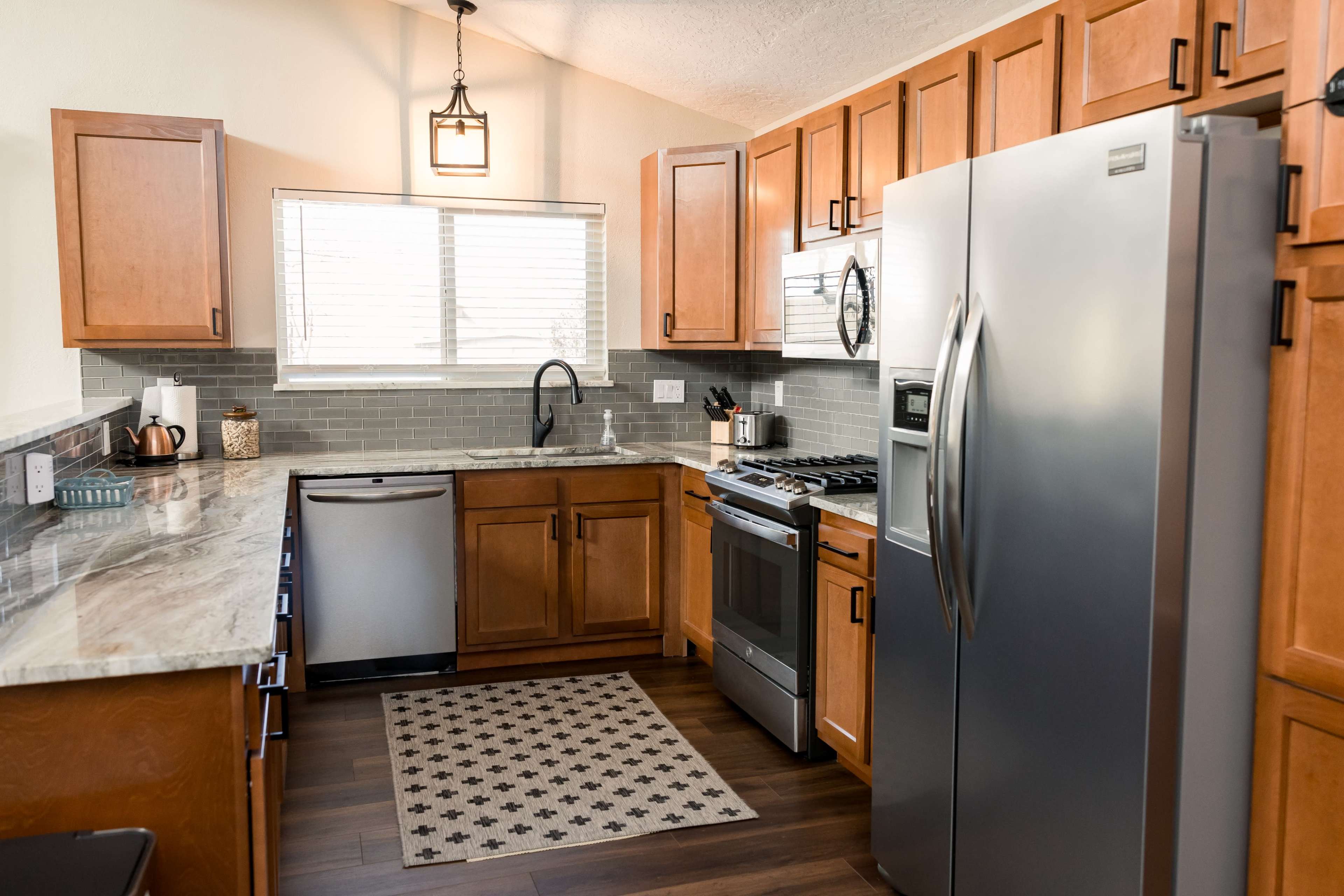 A modern kitchen with wooden cabinetry, stainless steel appliances, and a patterned rug on the floor.