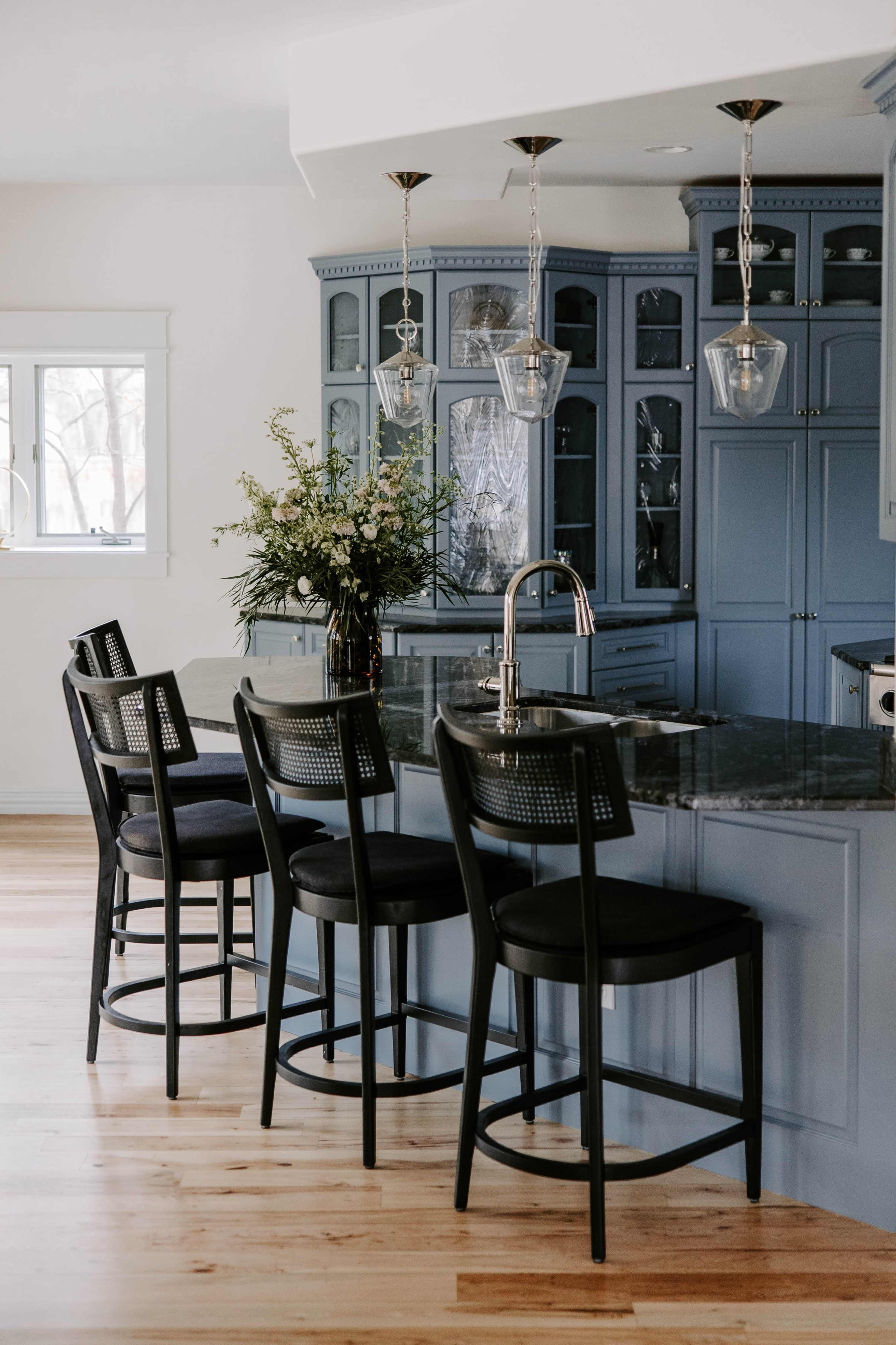 The image shows a modern kitchen featuring a blue cabinetry, a black granite countertop, and four bar stools at a kitchen island.
