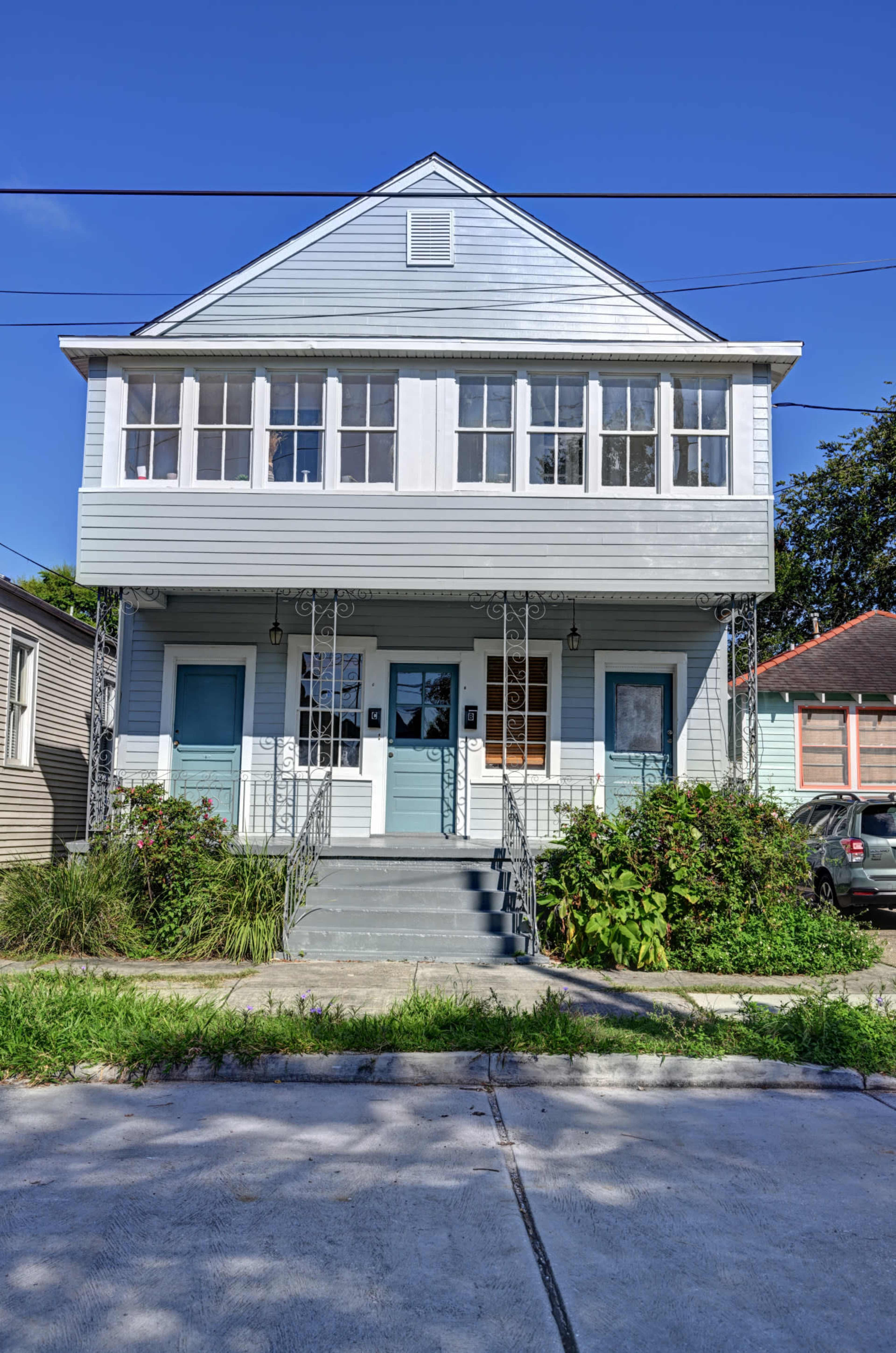 A two-story house with a light blue exterior features a front porch with decorative railings and two distinct entry doors.