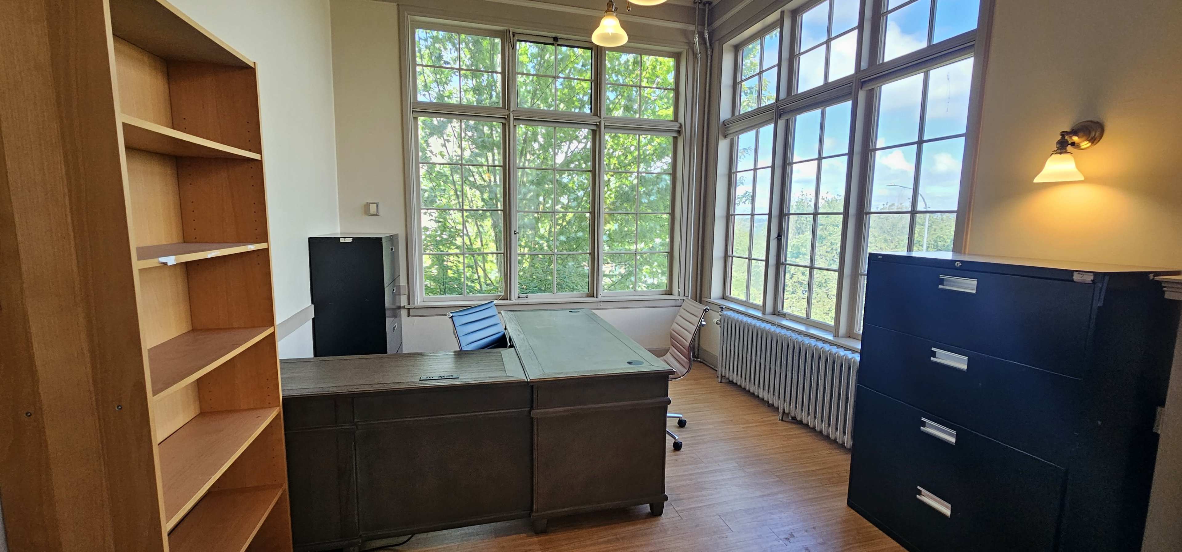 The image shows an office space with large windows, a desk, a rolling chair, a filing cabinet, and a bookshelf.