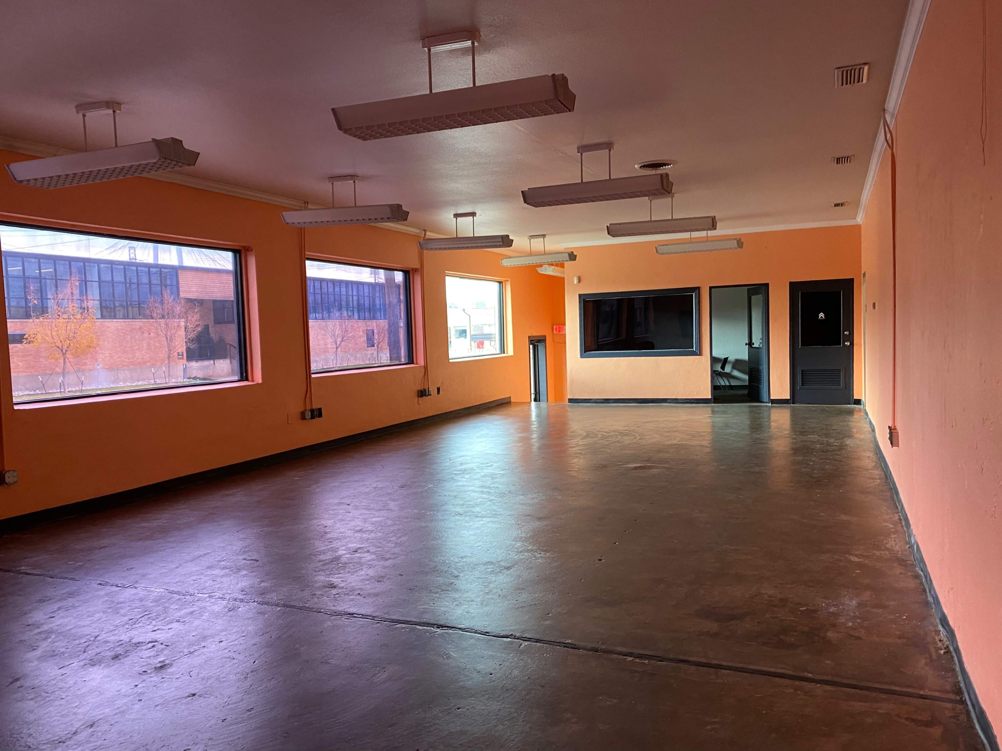 An empty room with orange walls, large windows, and a concrete floor.