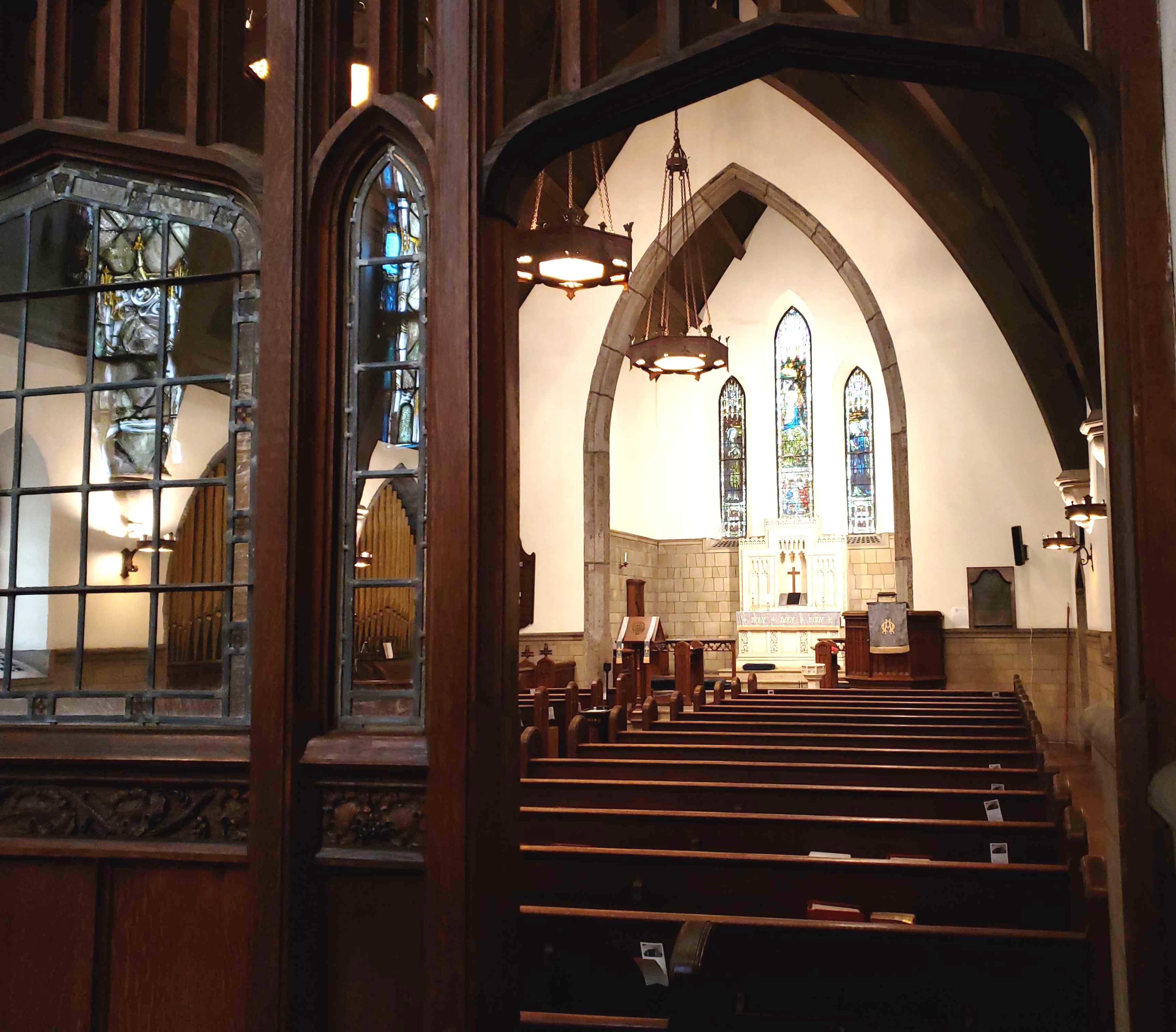 The image shows the interior of a church with wooden pews, stained glass windows, and an altar at the front.