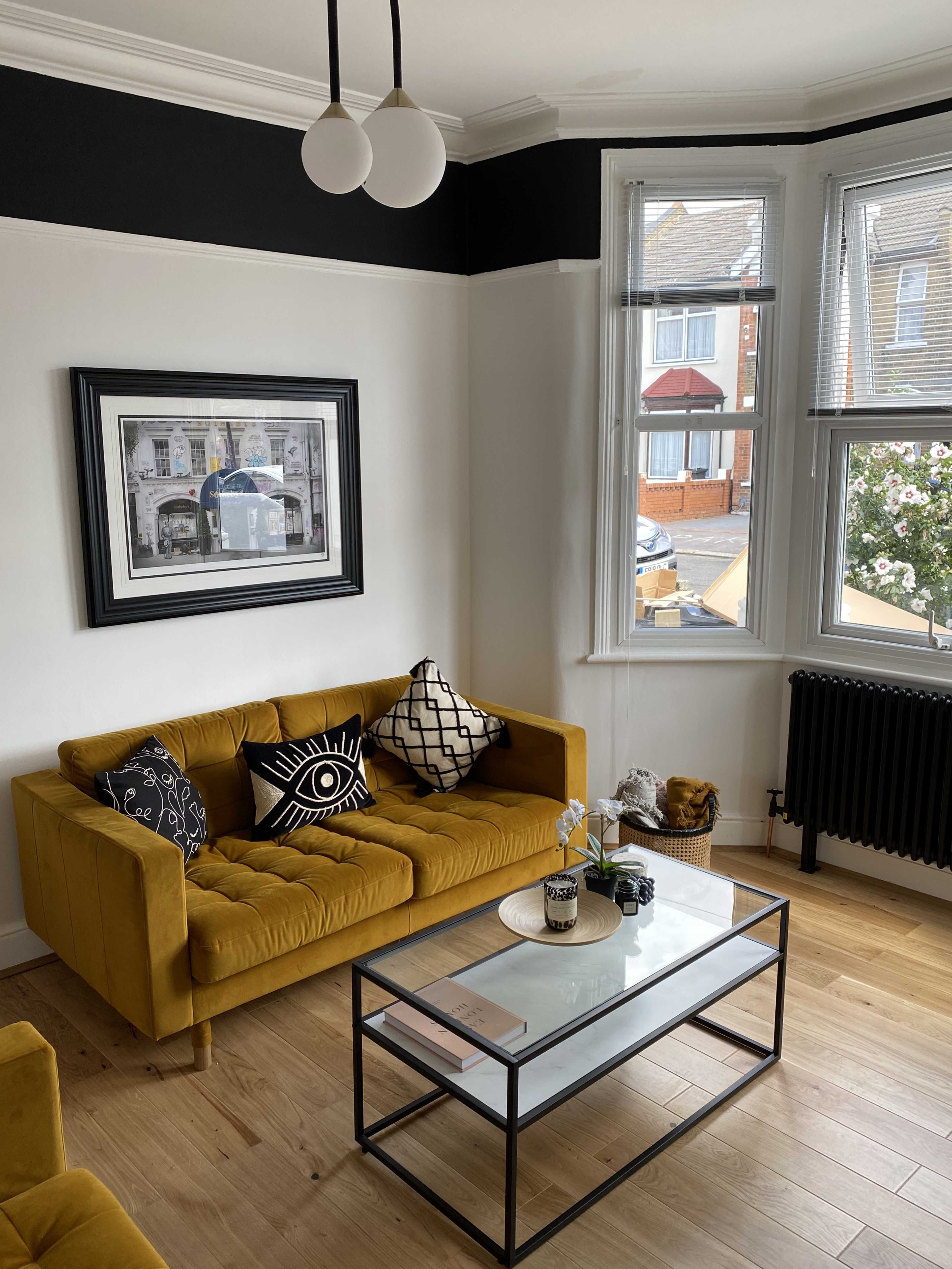 The room features a yellow sofa, a glass coffee table, and a large window with a view of the street outside.