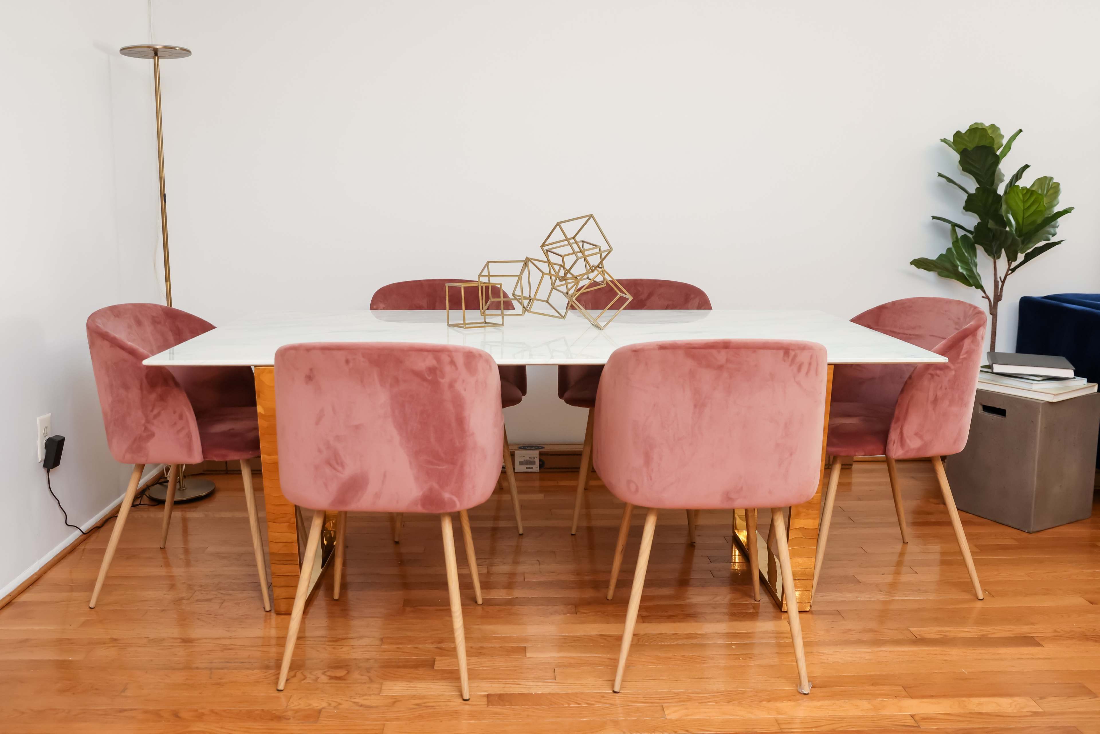 A rectangular dining table with a marble top is surrounded by six pink upholstered chairs, and a geometric sculpture is placed on the table.