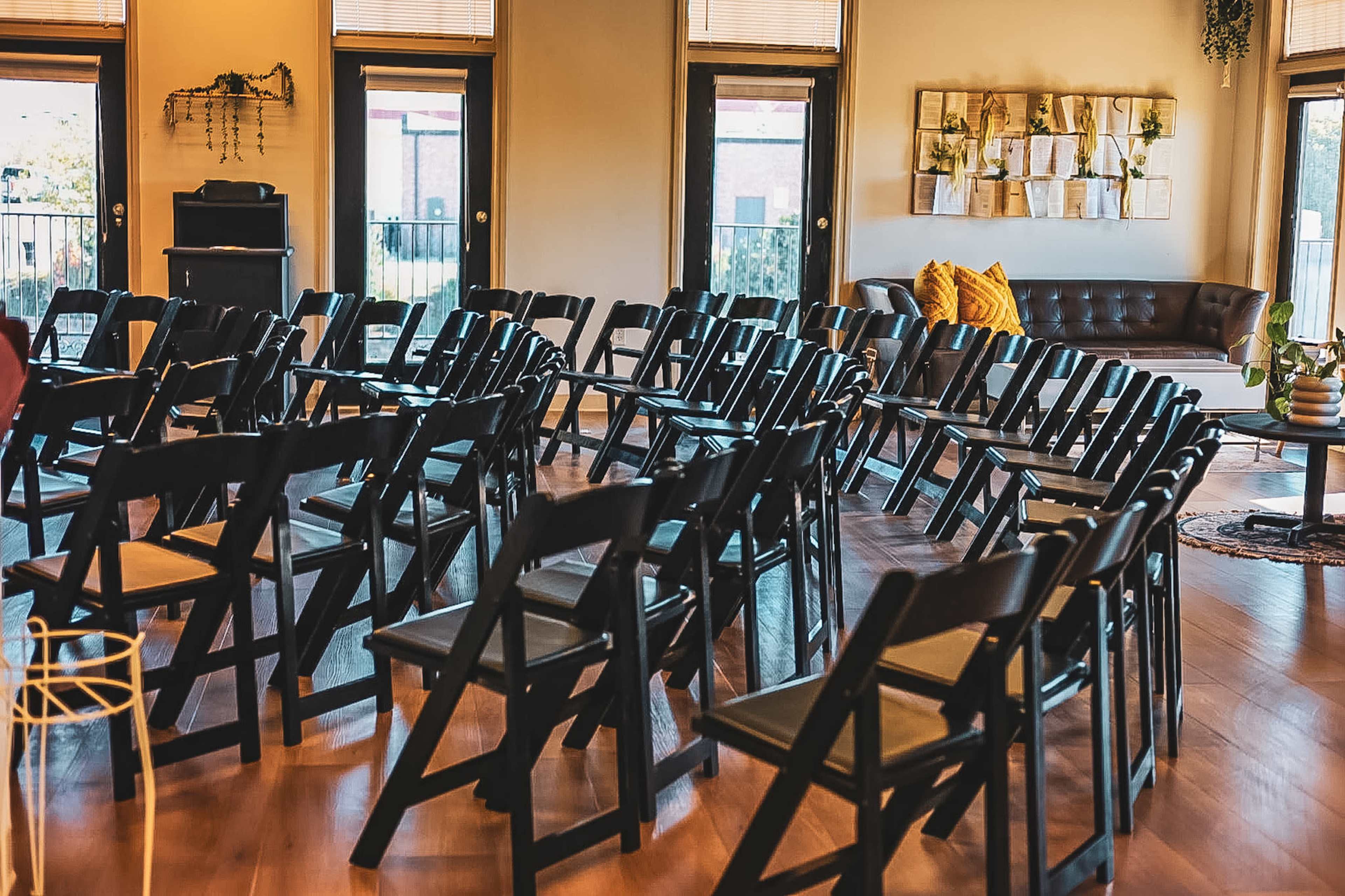 A room features several rows of black folding chairs arranged for an event, with a leather sofa and decorative wall art in the background.