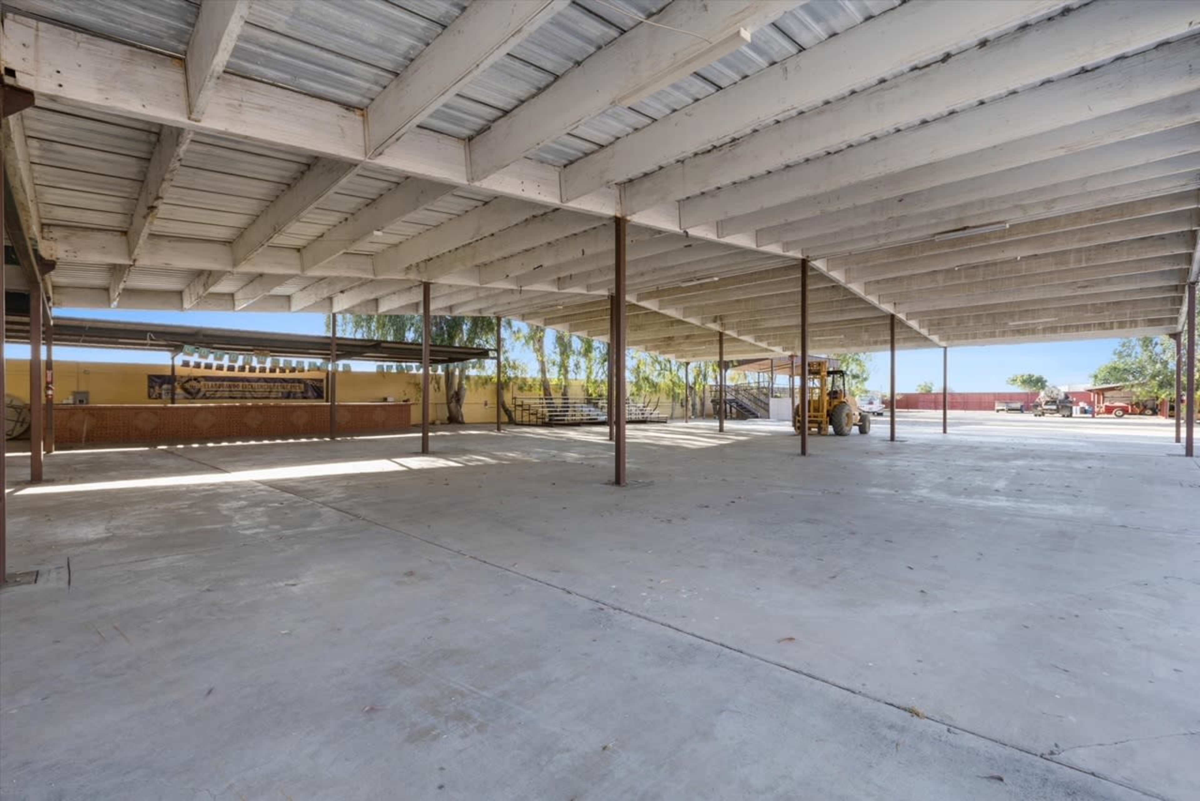 A large, open space under a metal roof with concrete flooring and steel supports, partially surrounded by walls.