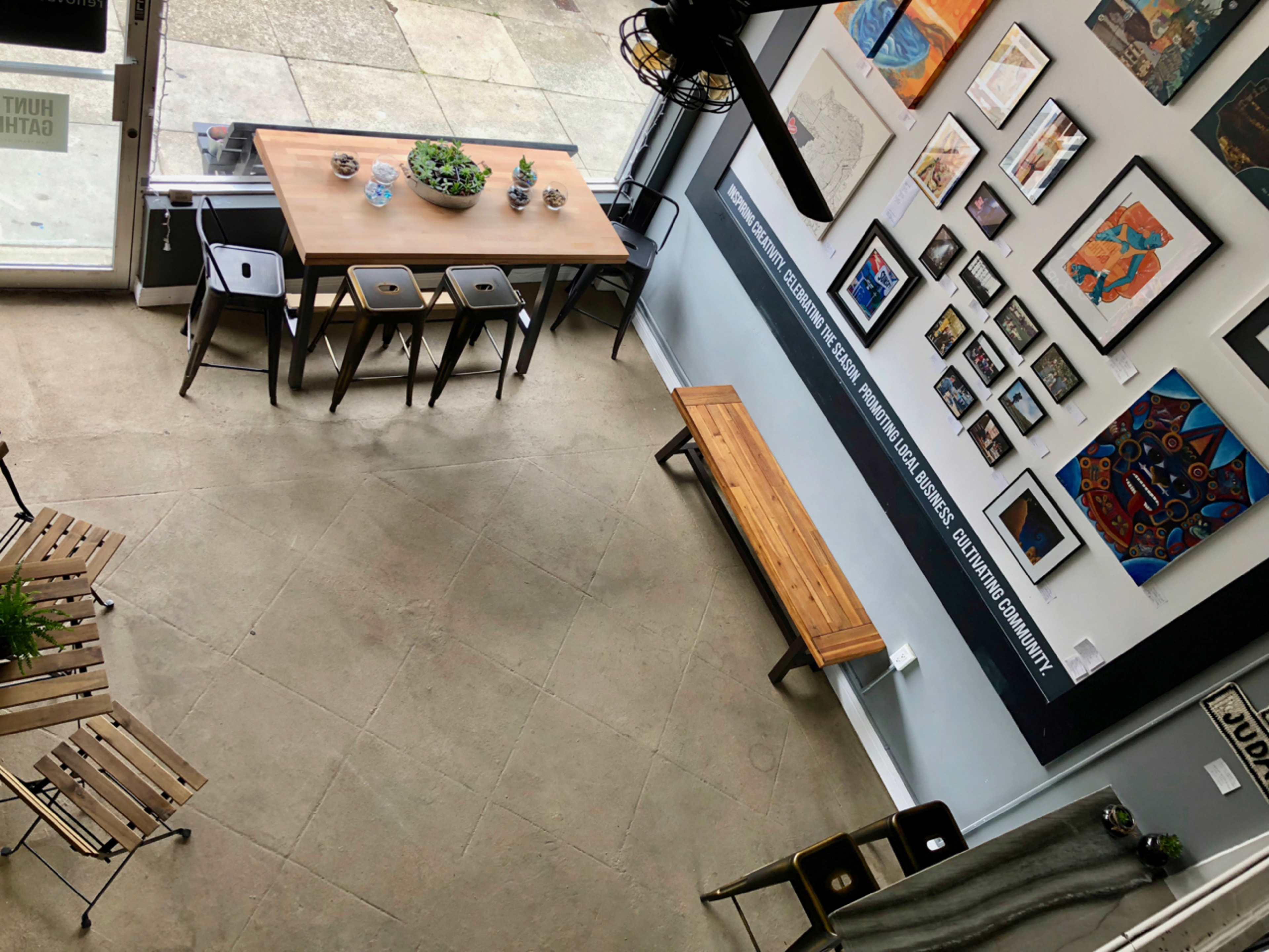 An indoor space featuring a wooden table surrounded by chairs, a bench, and various artworks displayed on the walls.