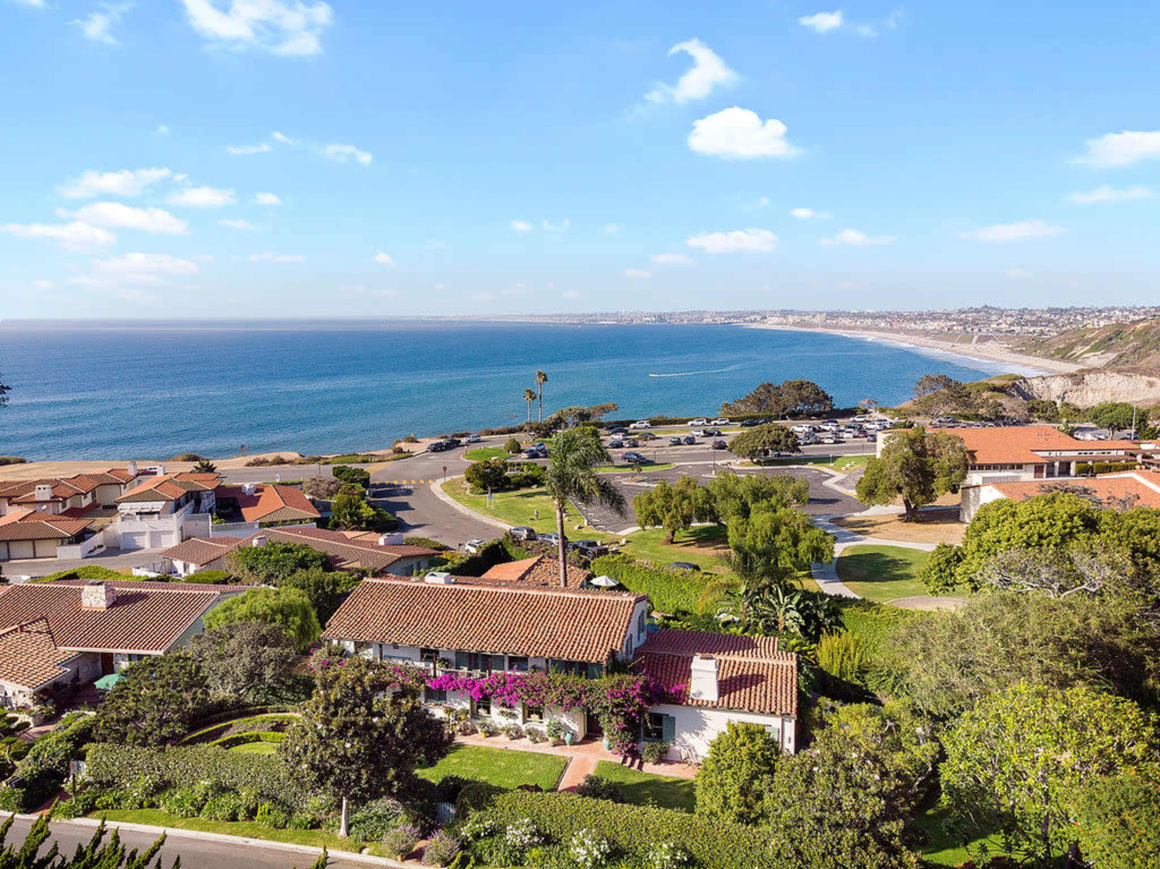 The image shows a coastal view with houses overlooking a beach and a winding road lined with greenery.