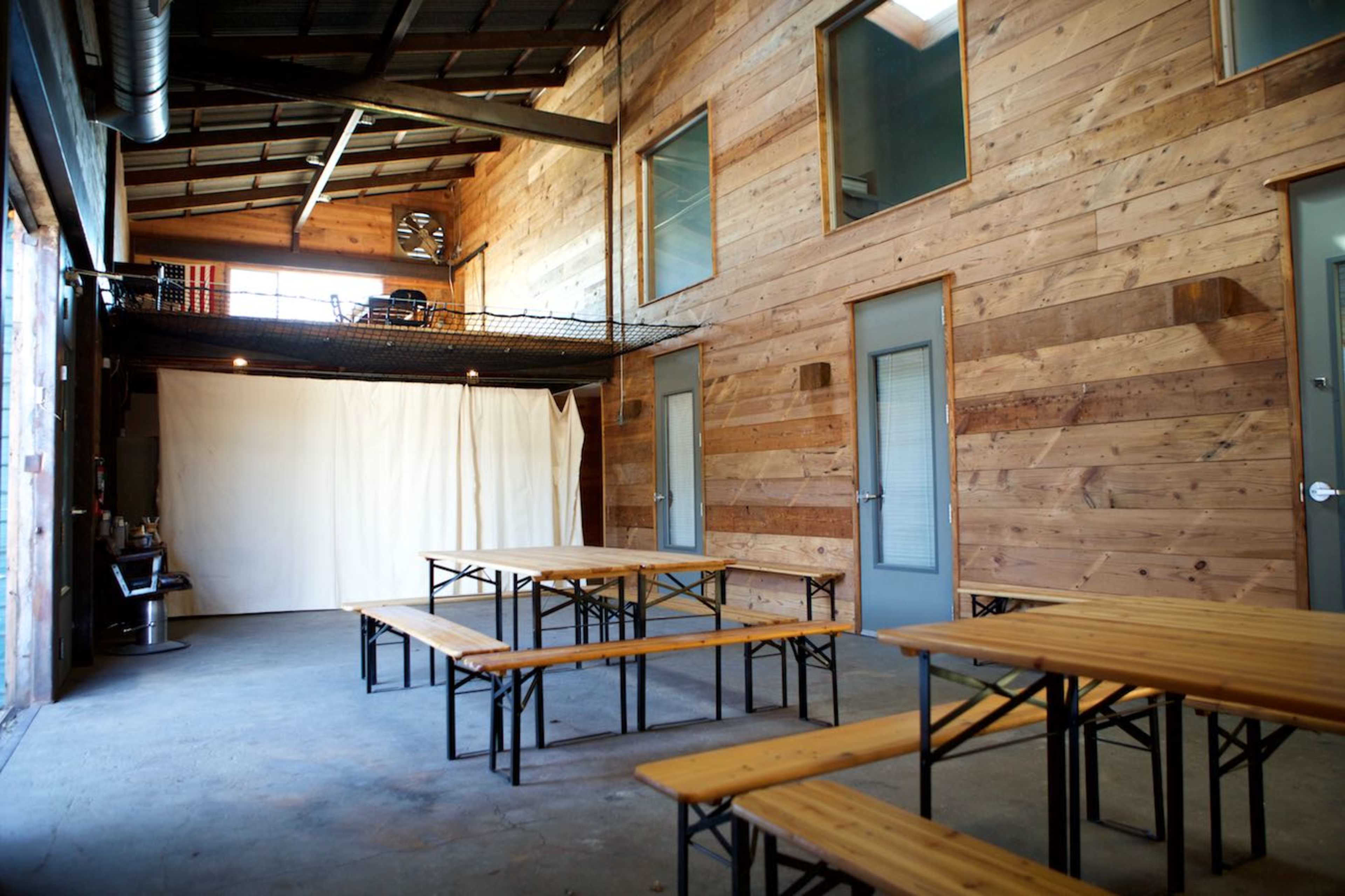 The image shows an indoor space with wooden walls, multiple wooden tables, and a loft area above.