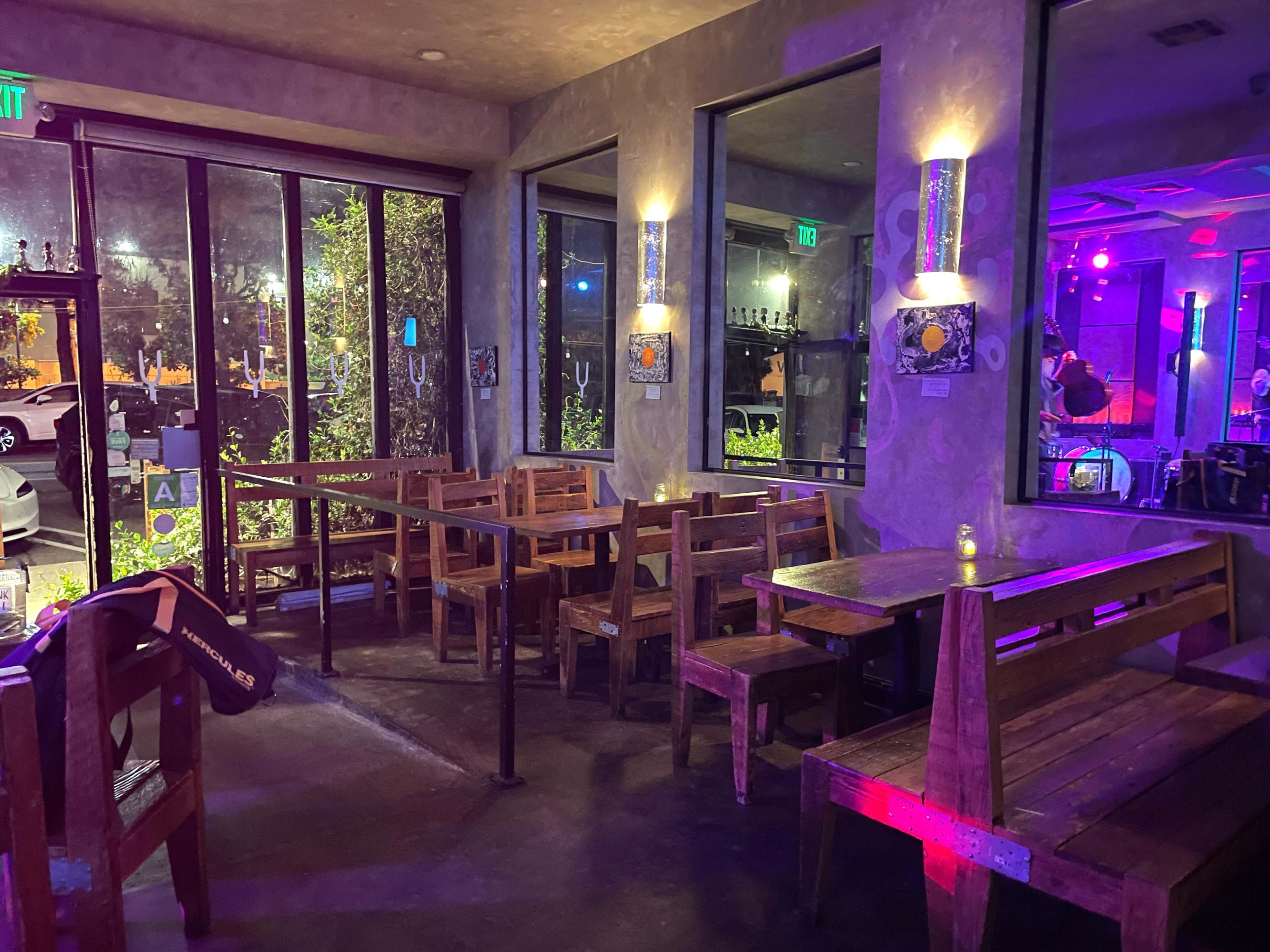 The image shows a dimly lit restaurant interior with wooden tables and chairs arranged near large windows.