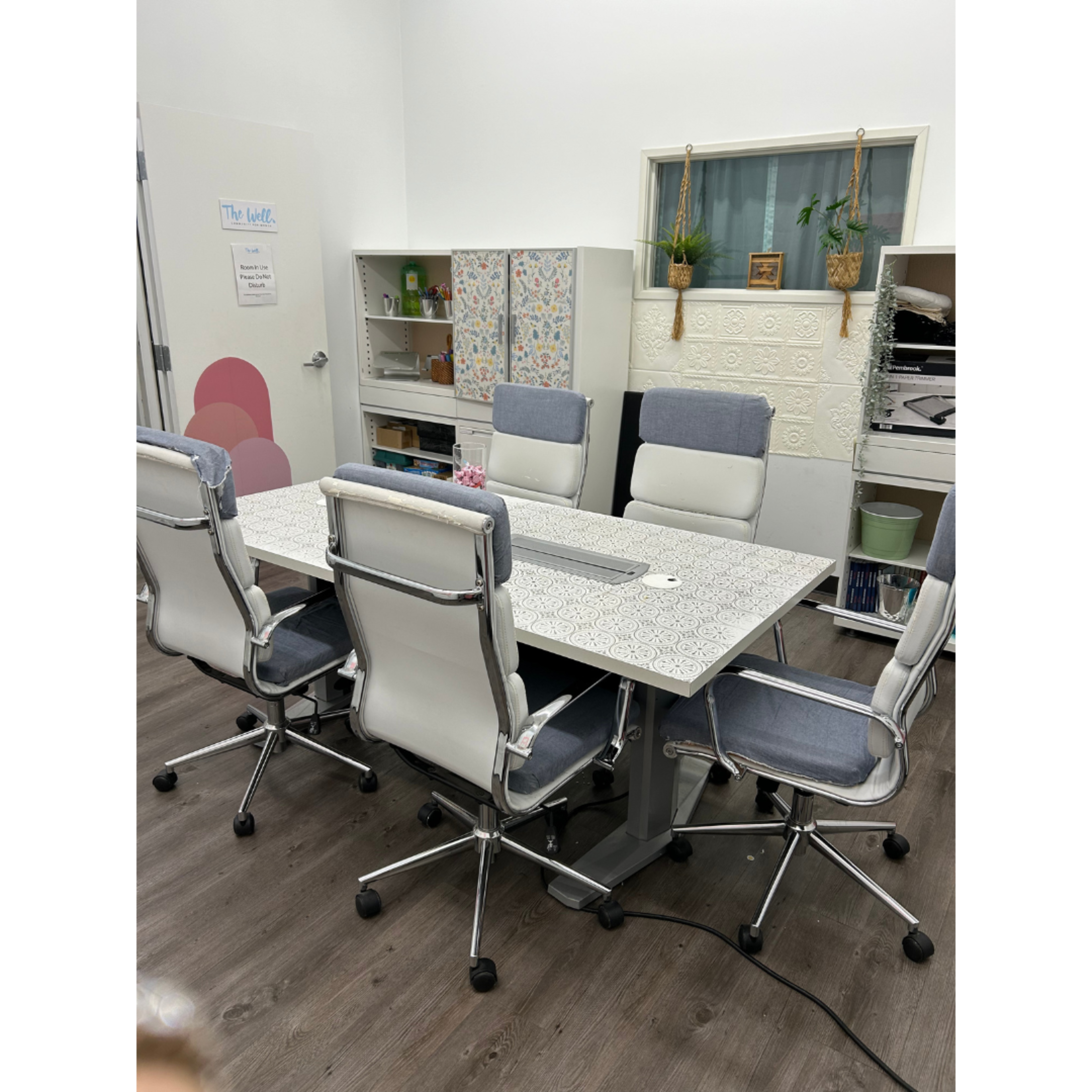 The image shows a modern conference room with a large table surrounded by six ergonomic chairs and storage cabinets in the background.