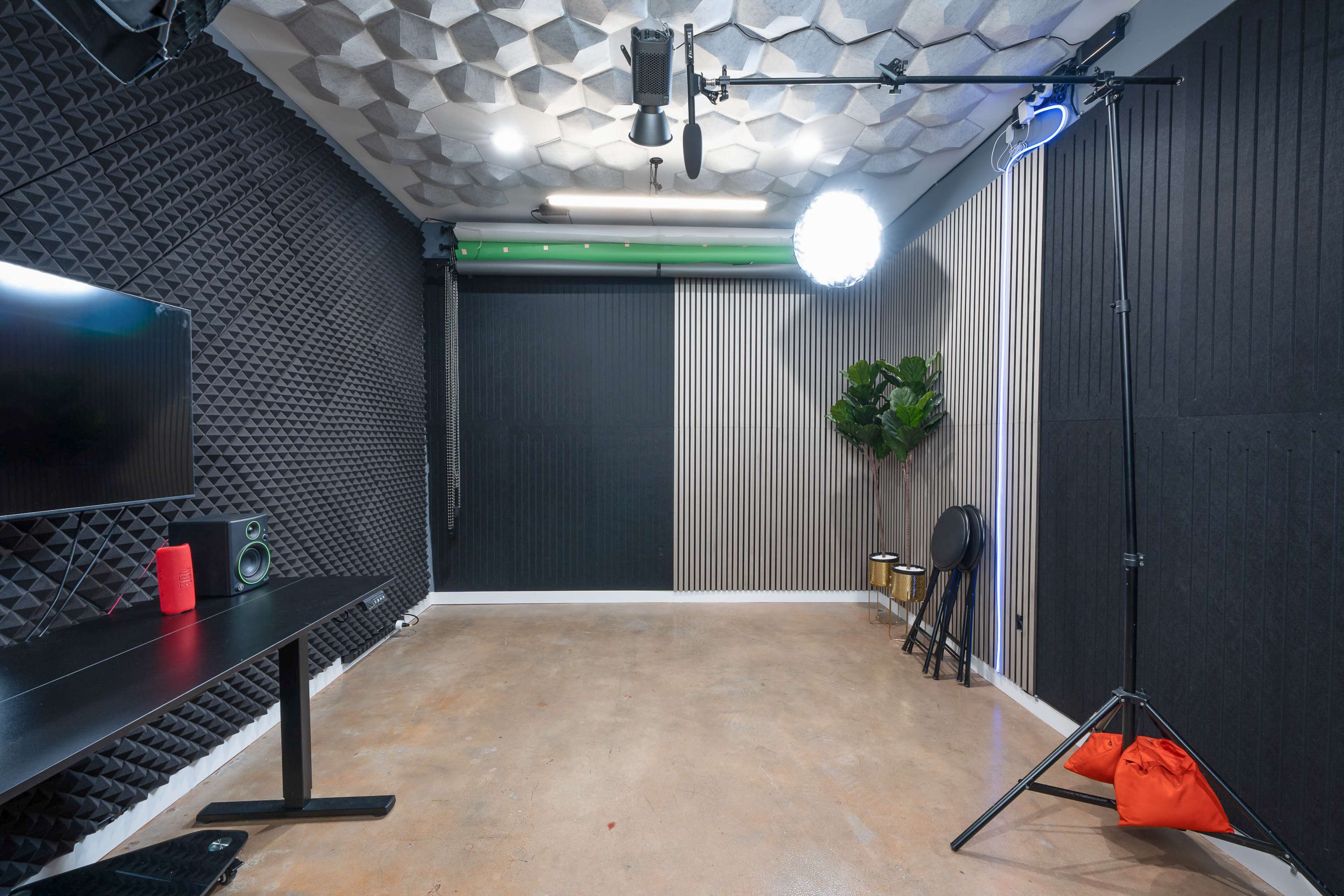 The image shows a vacant studio space with acoustic wall panels, a mounted light, and a television on a black table.