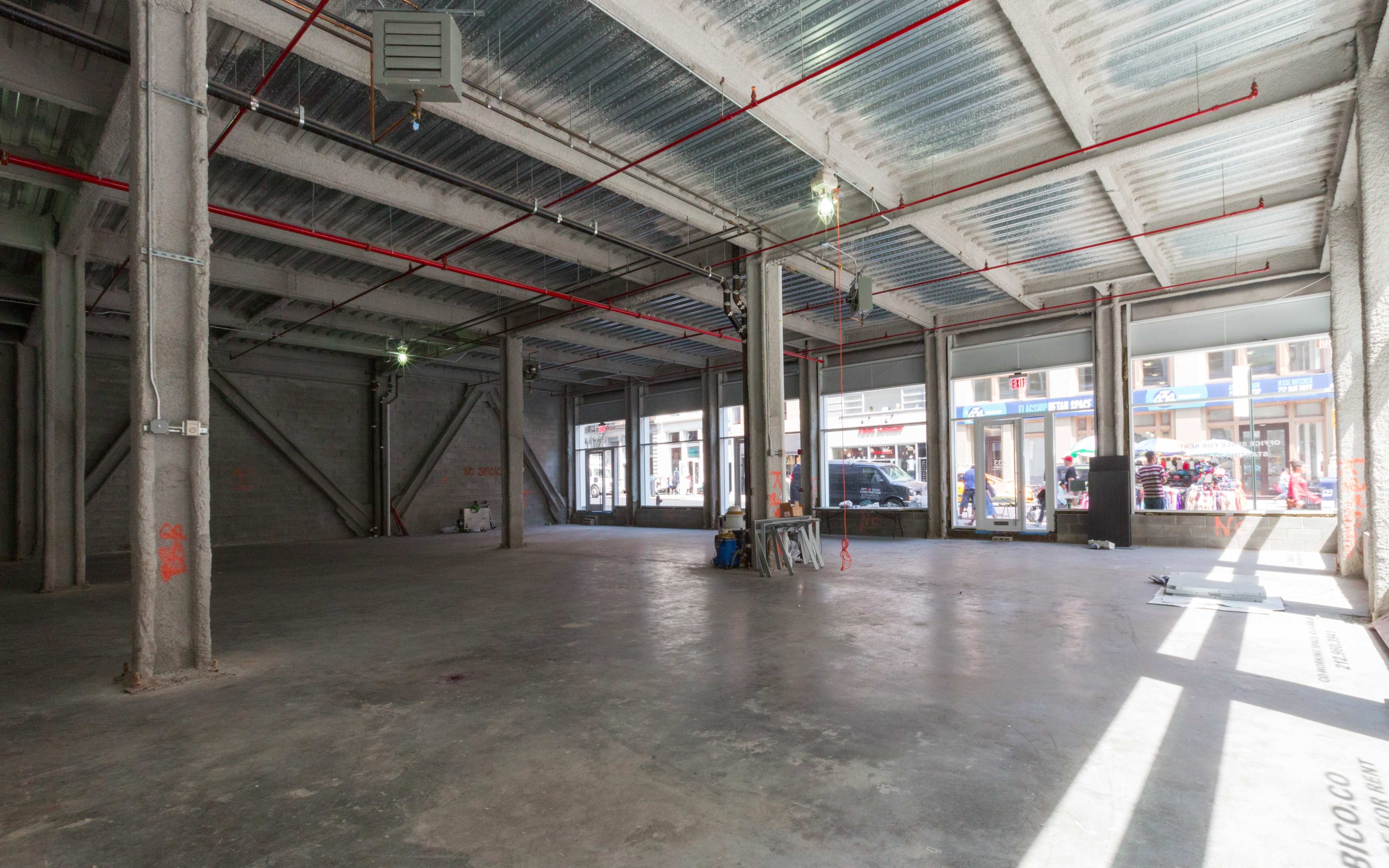 An empty commercial space with exposed concrete walls, high ceilings, and large windows allowing natural light to enter.