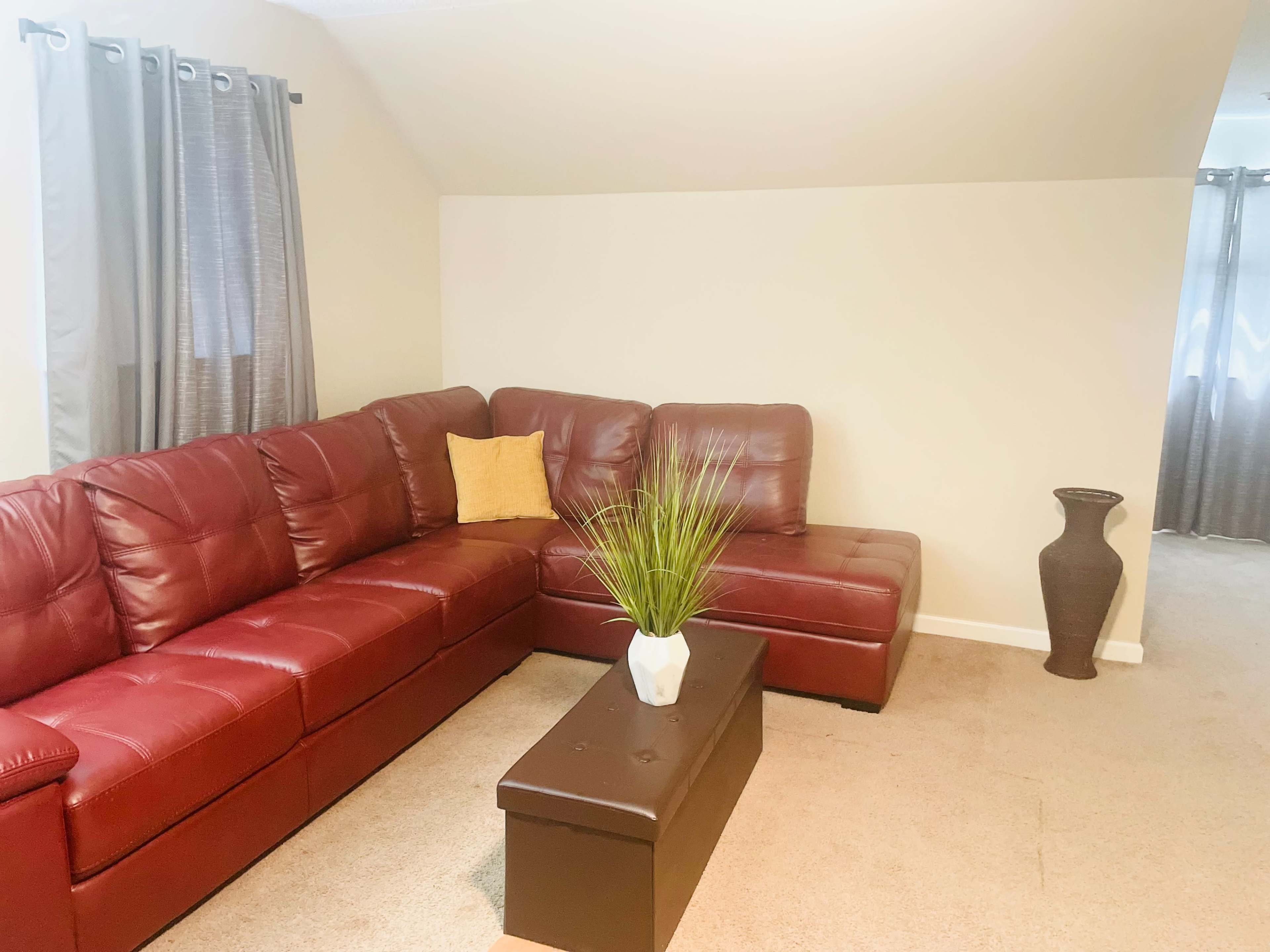 The room features a red sectional sofa, a coffee table with a plant, and a decorative vase against a light-colored wall.