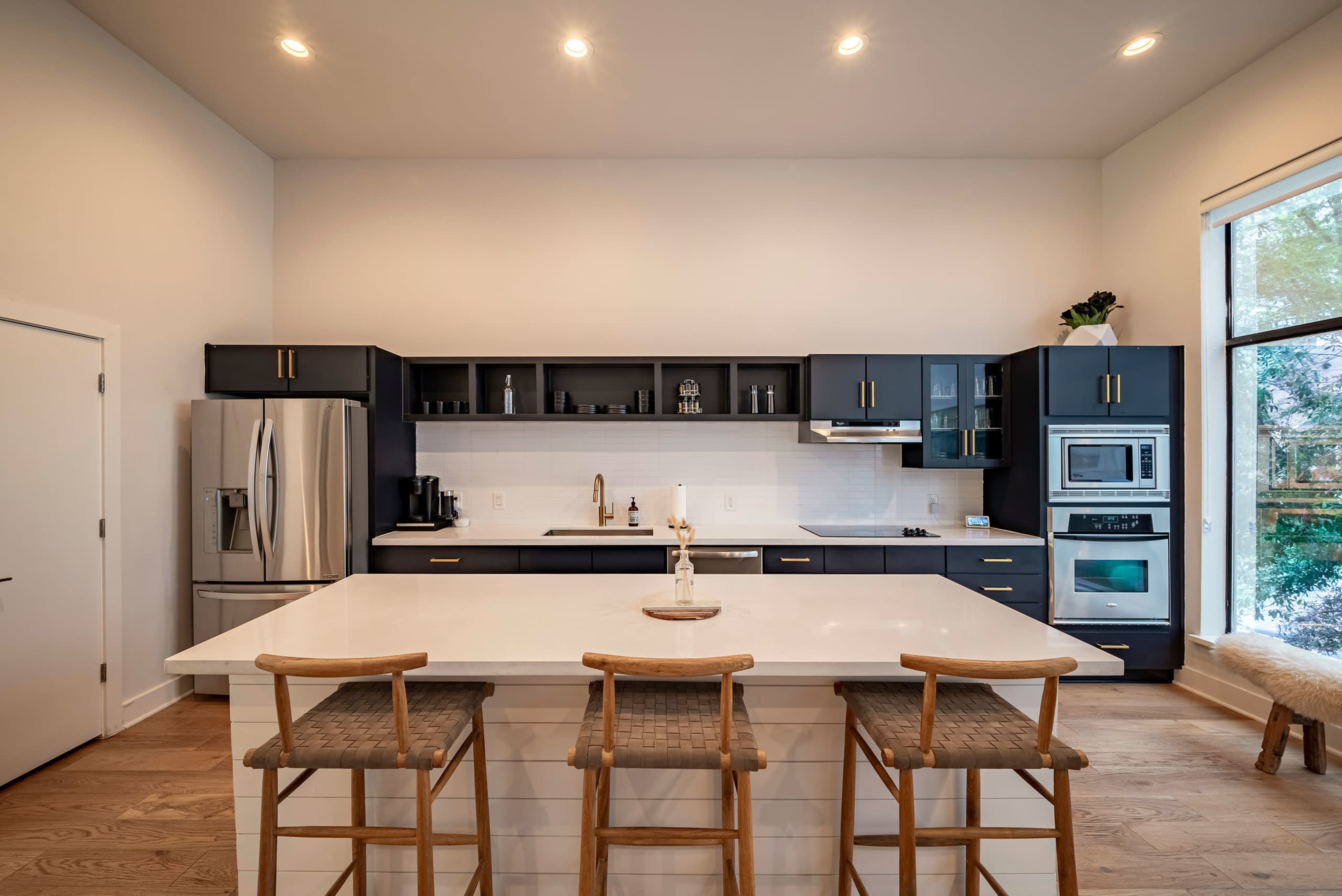 A modern kitchen featuring a large island, black cabinetry, stainless steel appliances, and a bright, airy atmosphere.