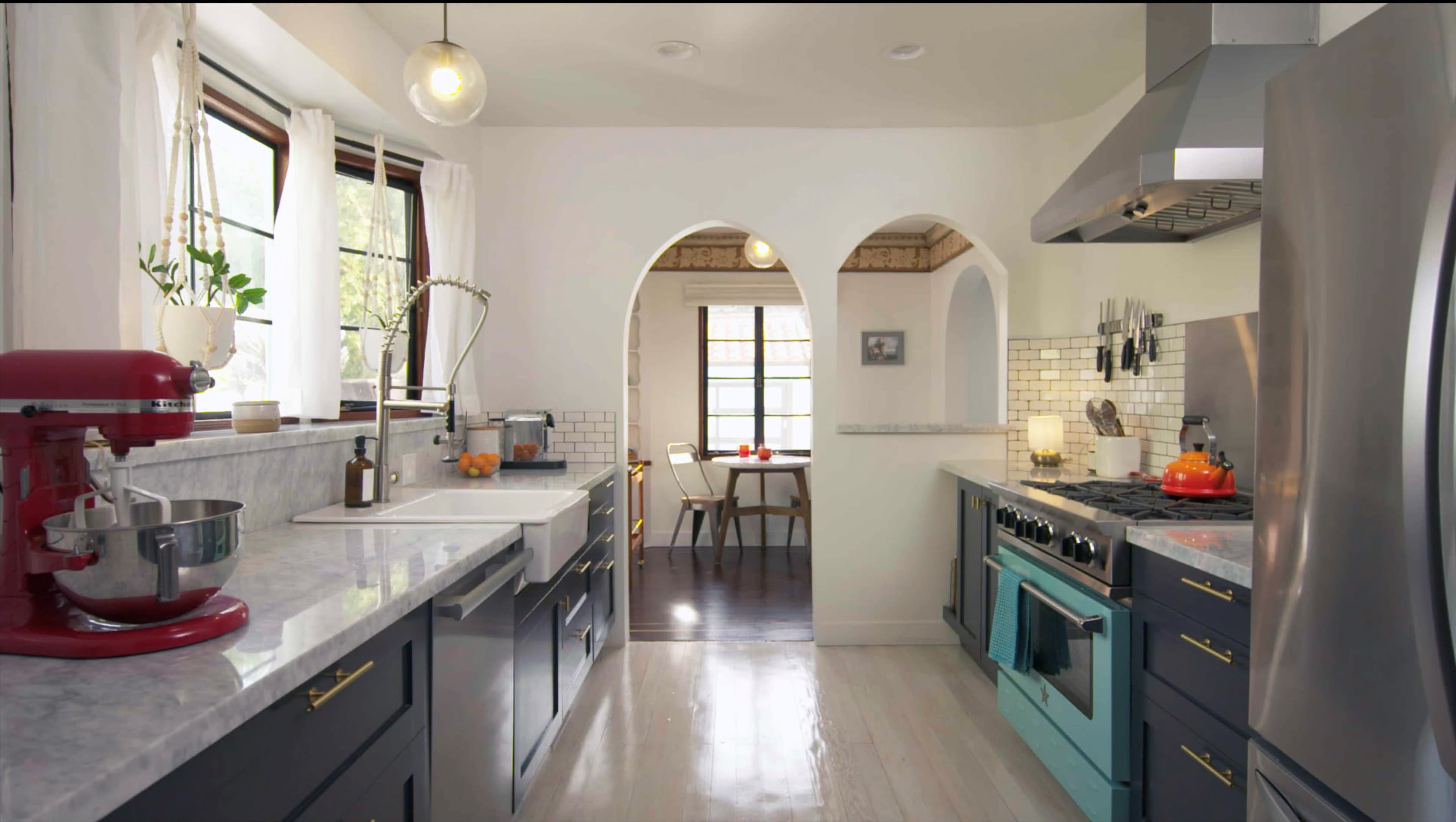 A modern kitchen features marble countertops, dark cabinetry, an aqua blue stove, and arched doorways leading to a dining area.