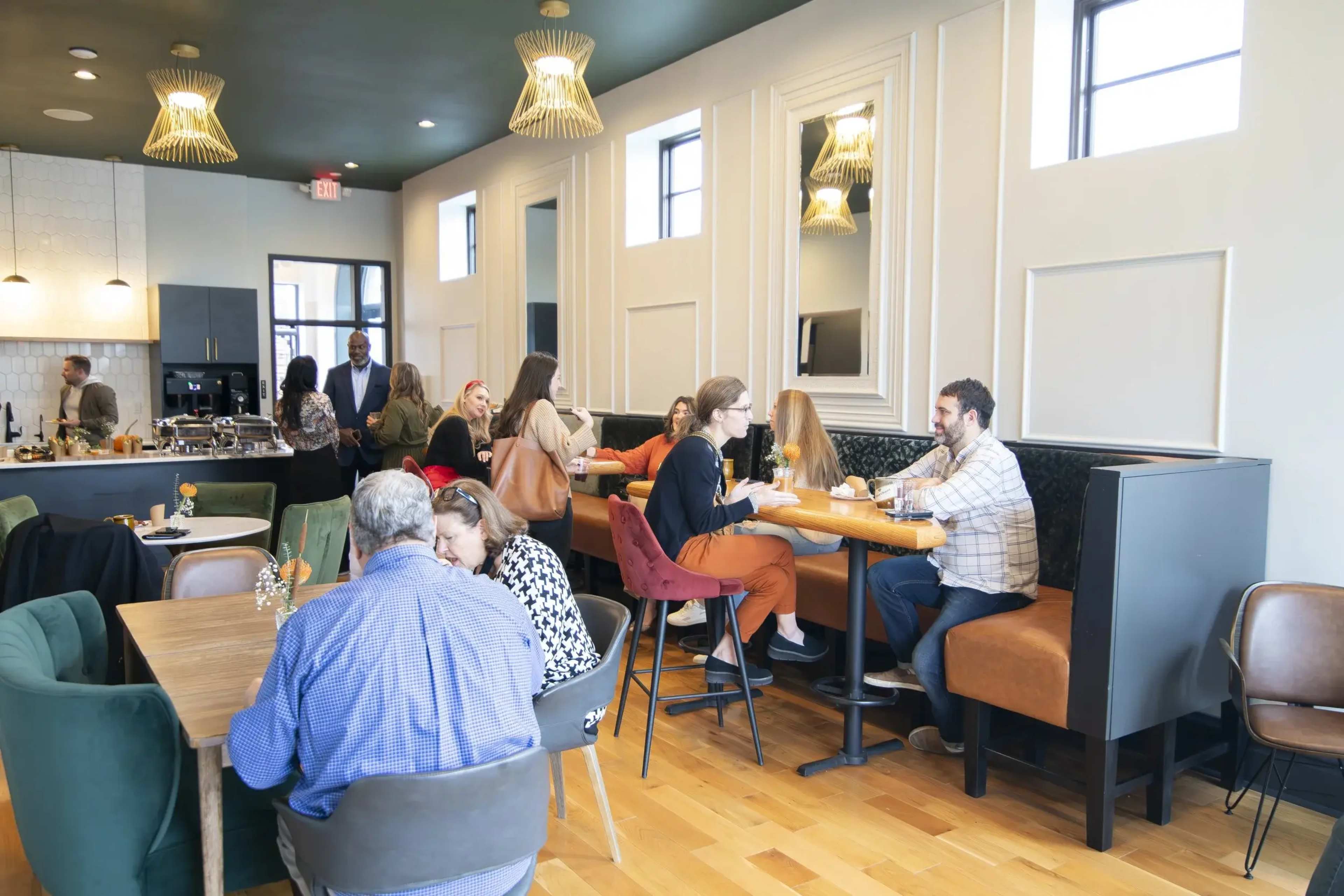 The image shows a modern restaurant interior with several groups of people dining at tables and a bar area in the background.