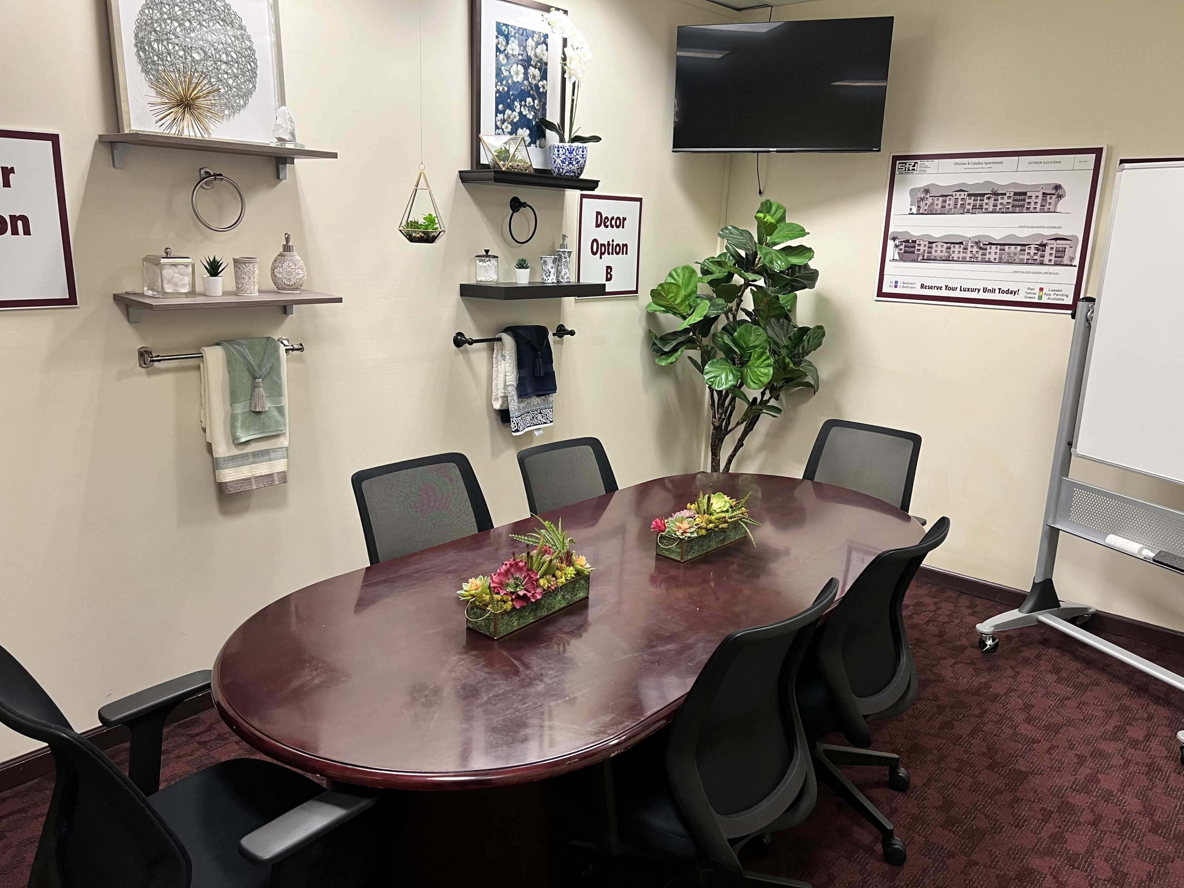 A conference room features a large round table surrounded by black chairs, with decor and plants displayed on shelves and walls.