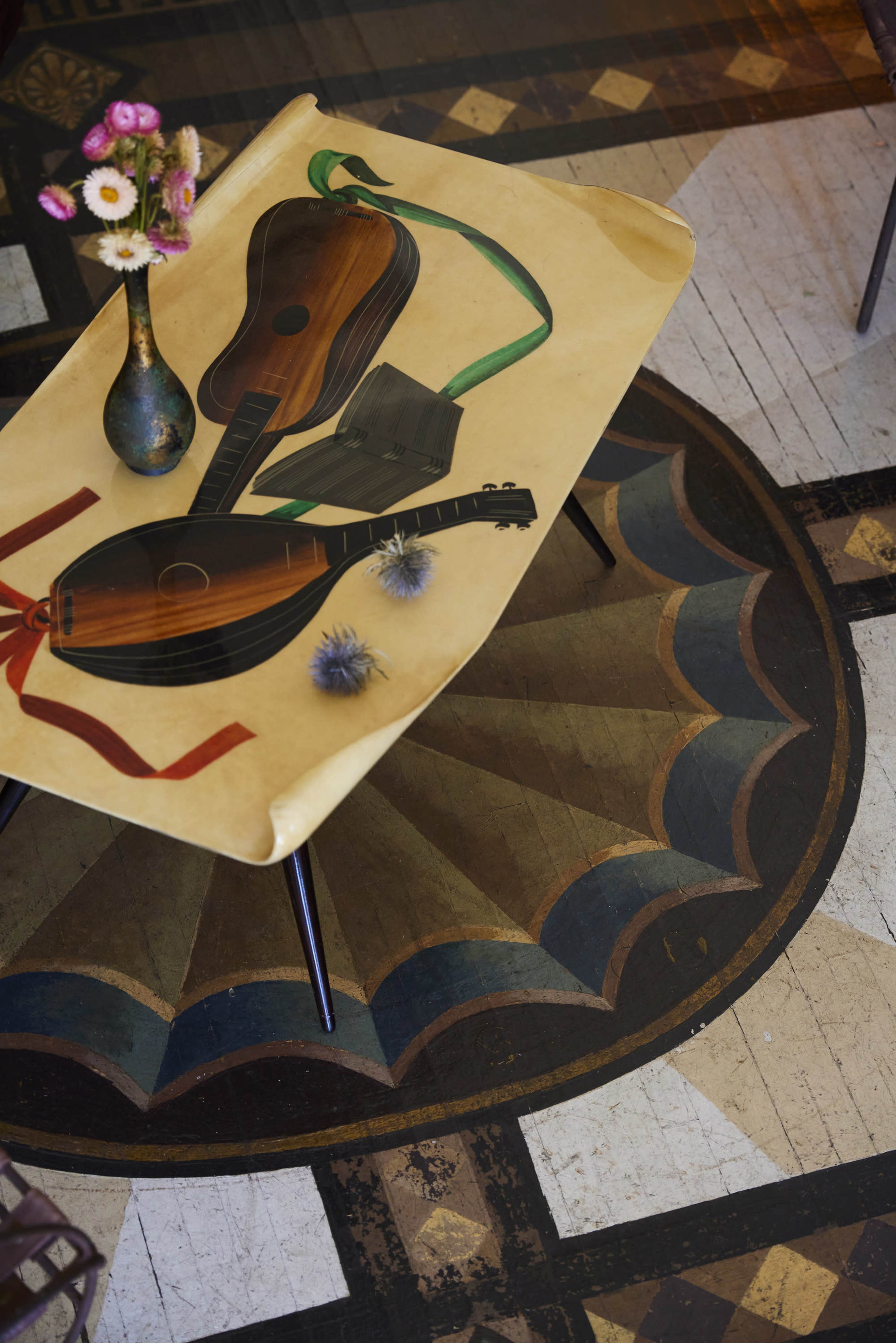 A tabletop featuring painted musical instruments is placed on a patterned wooden floor.