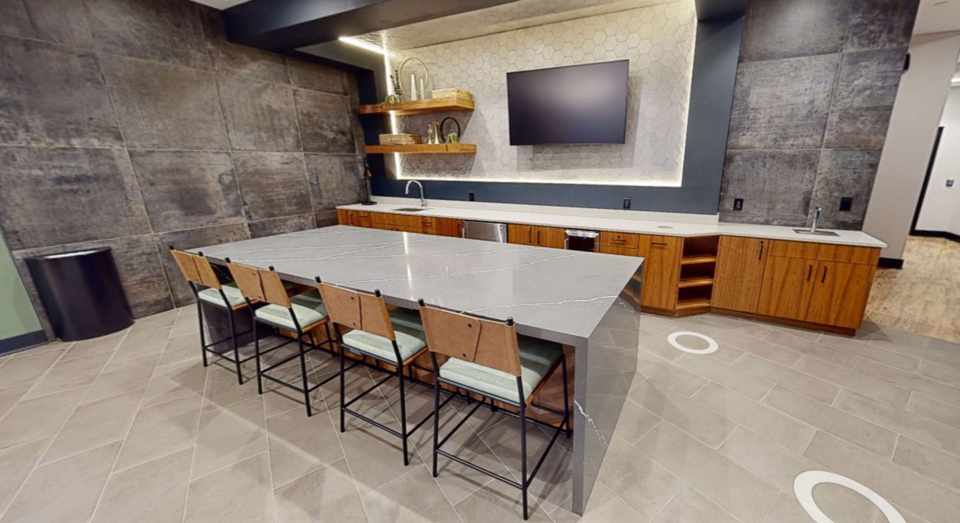 The image shows a modern kitchen with a large gray island and wooden cabinets, featuring a wall-mounted television above a countertop.