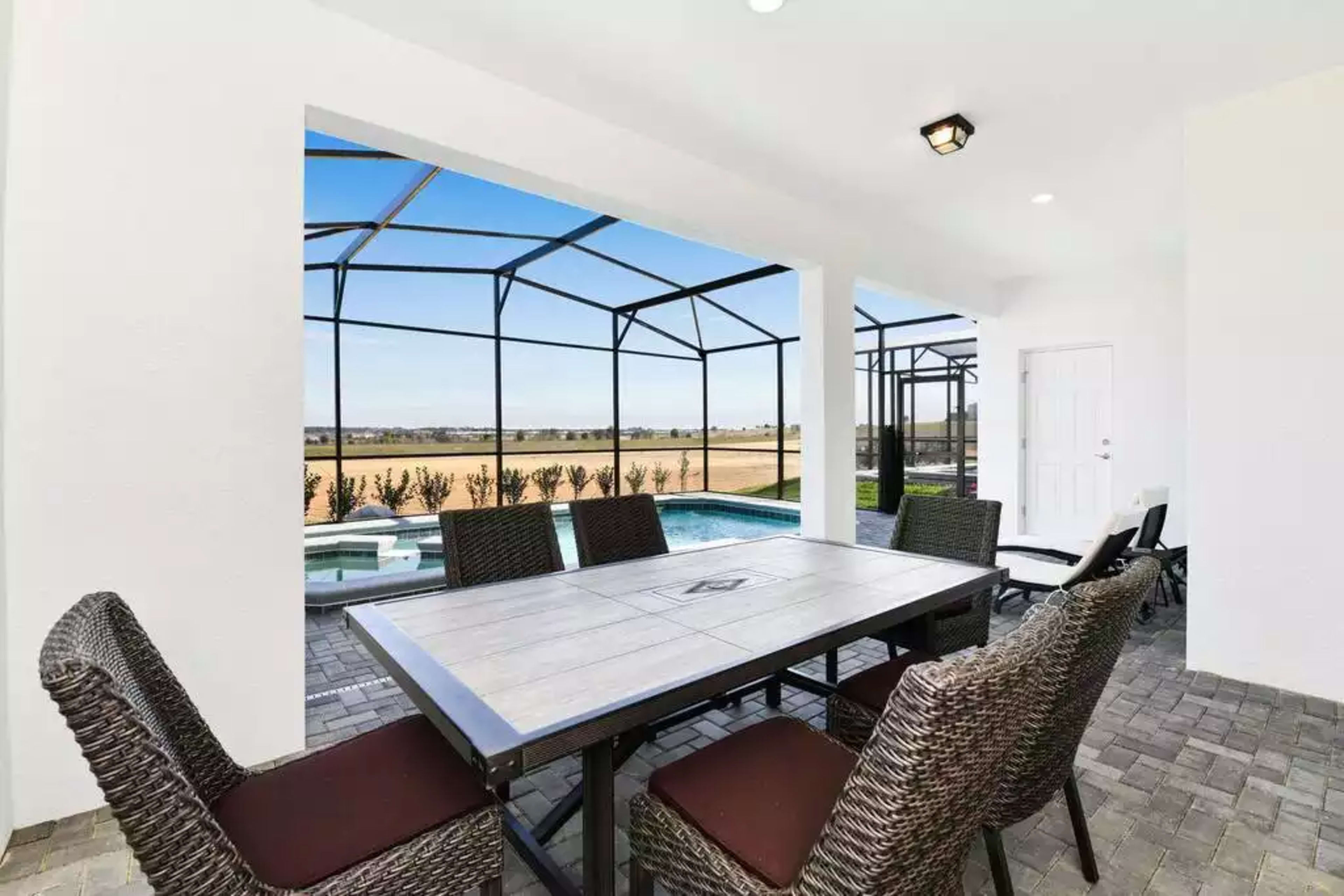 A patio with a table and chairs overlooks a pool area and an open landscape through a screened enclosure.