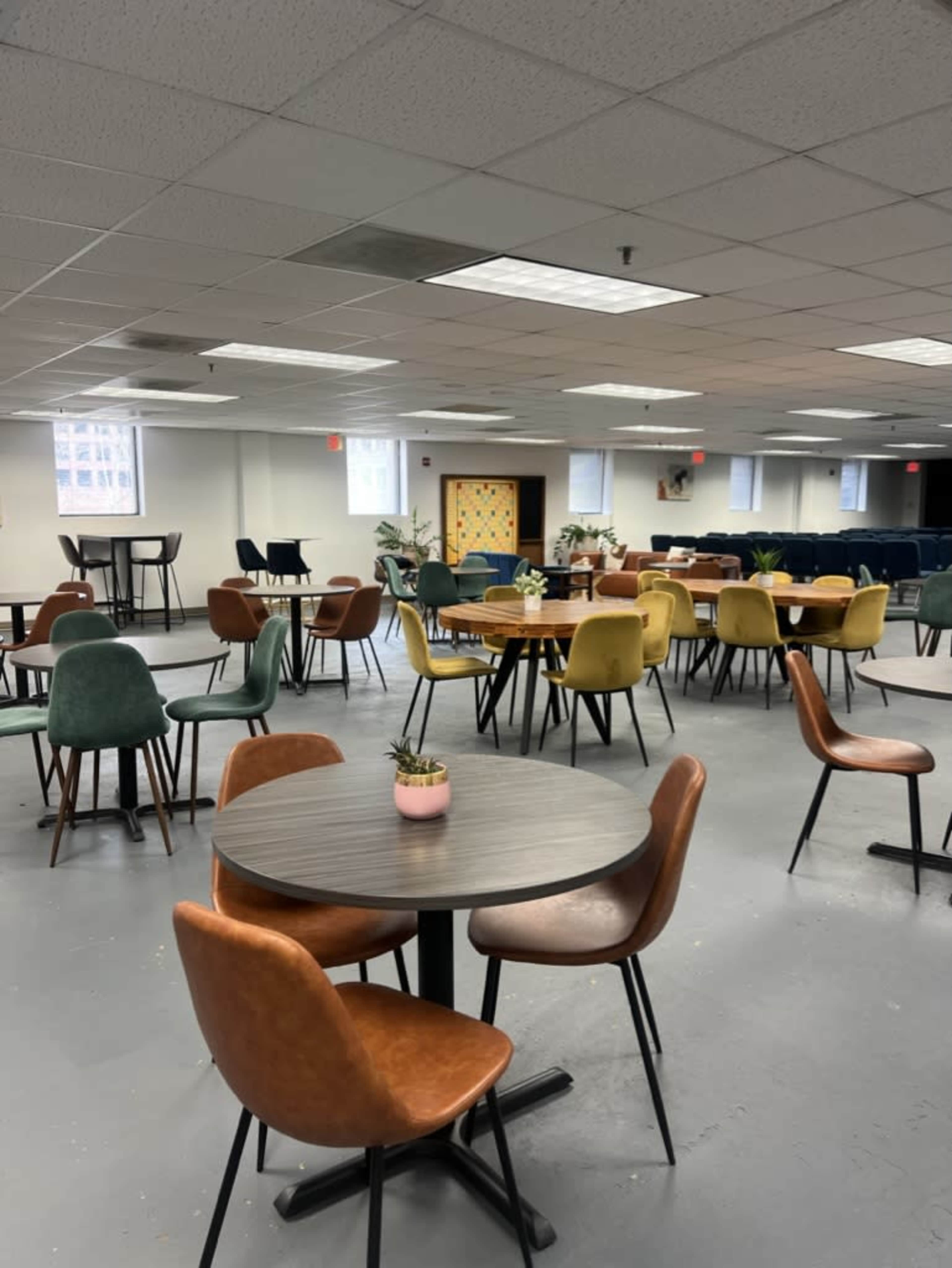 The image shows a spacious room with multiple tables and chairs arranged in various colors, designed for dining or gatherings.