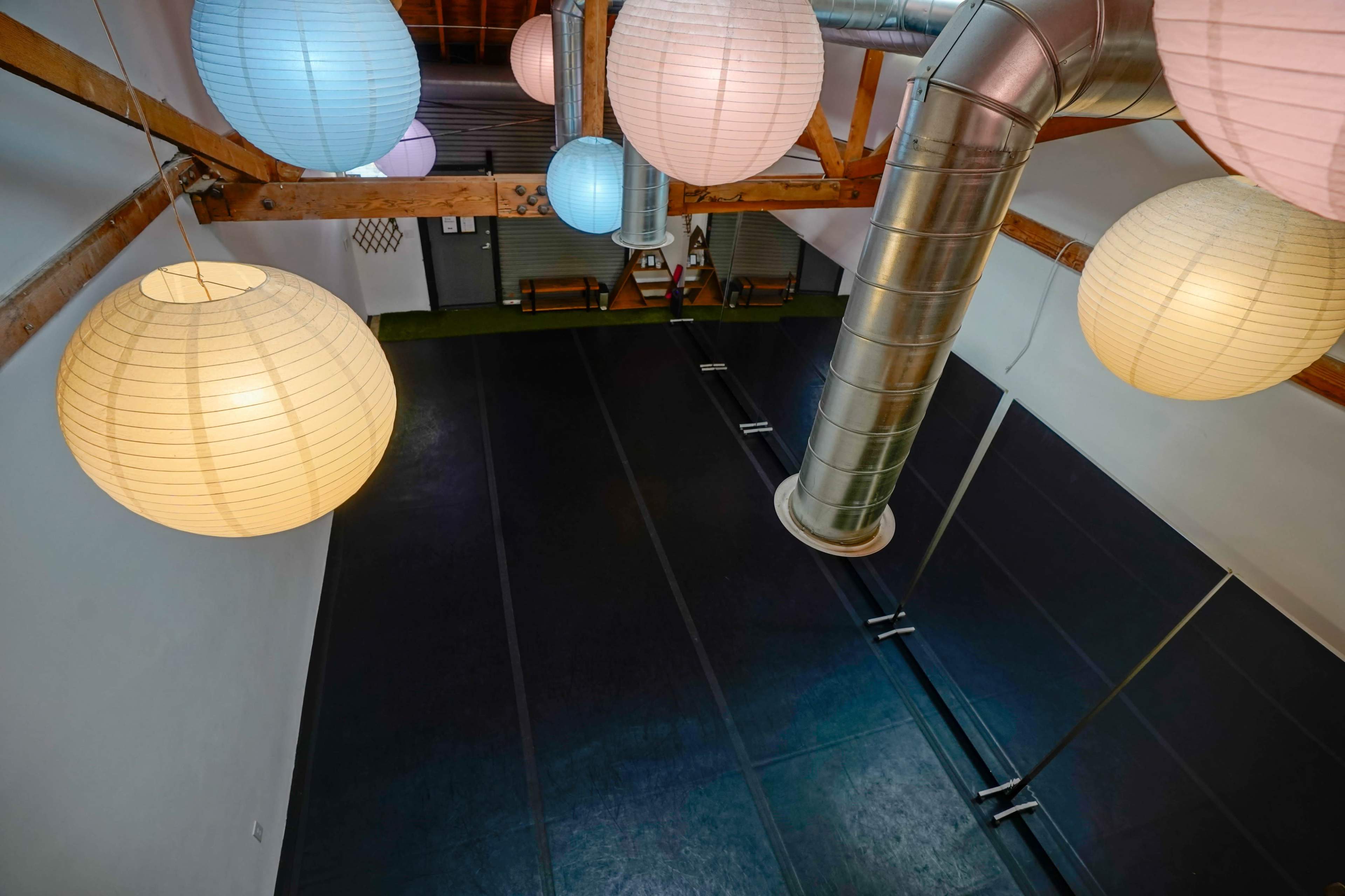 A spacious indoor area with a black floor, wooden beams, and large paper lanterns hanging from the ceiling.
