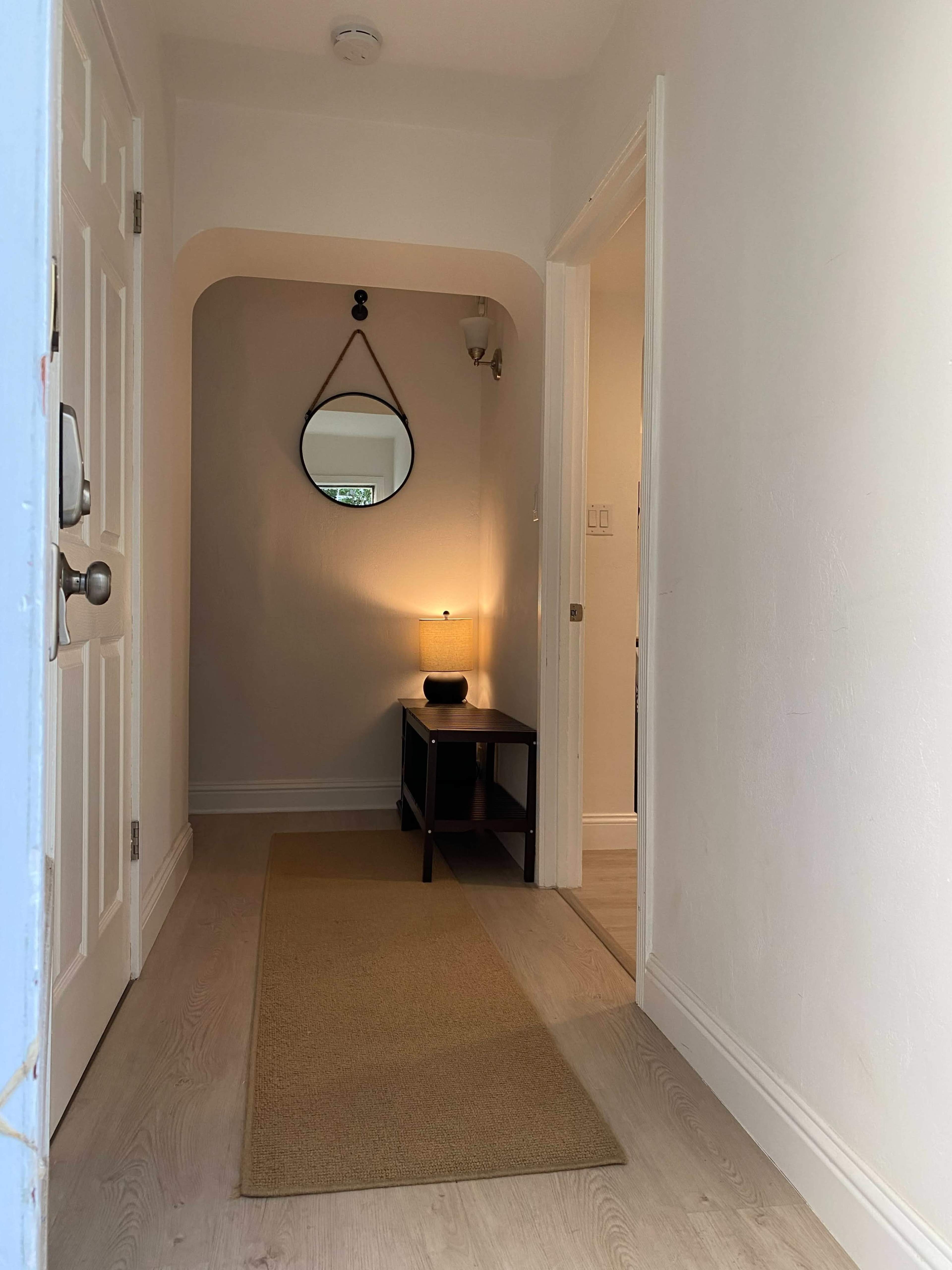 A narrow hallway with a round mirror, a small table, and soft lighting at the end.