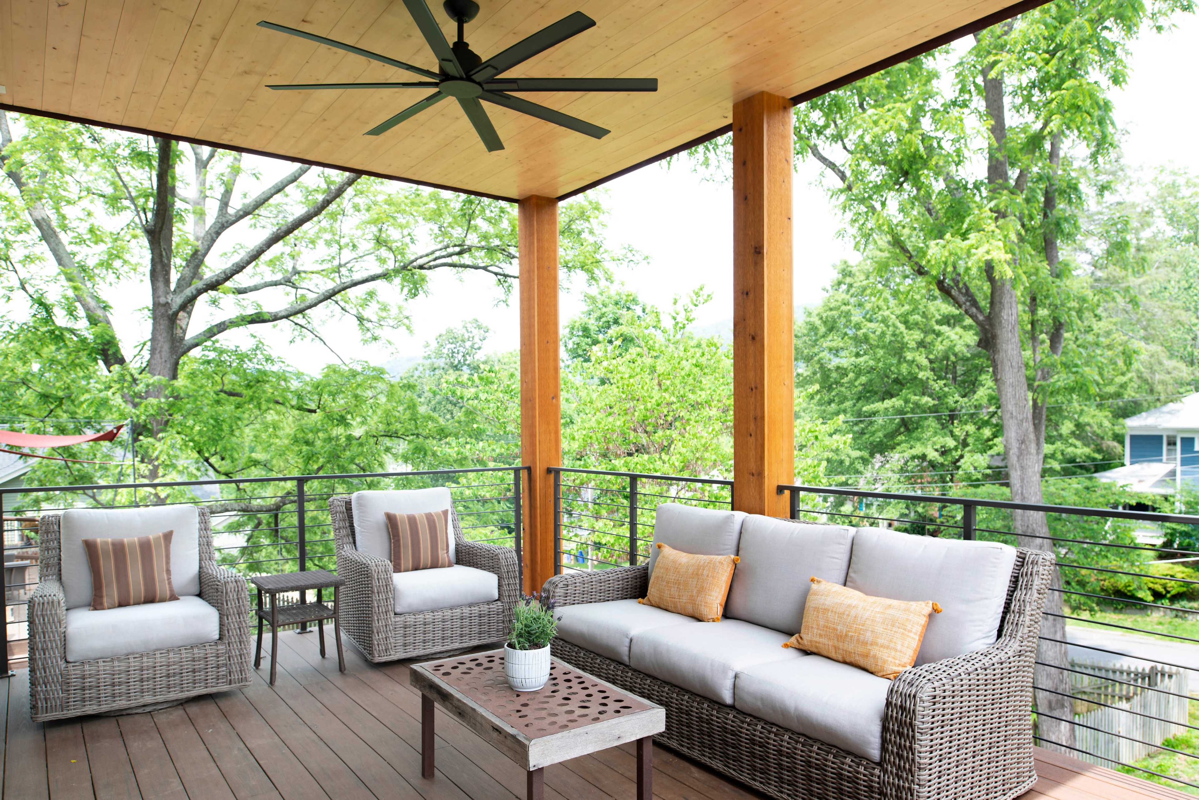 A covered porch with a seating area that includes a sofa and two chairs, surrounded by greenery.