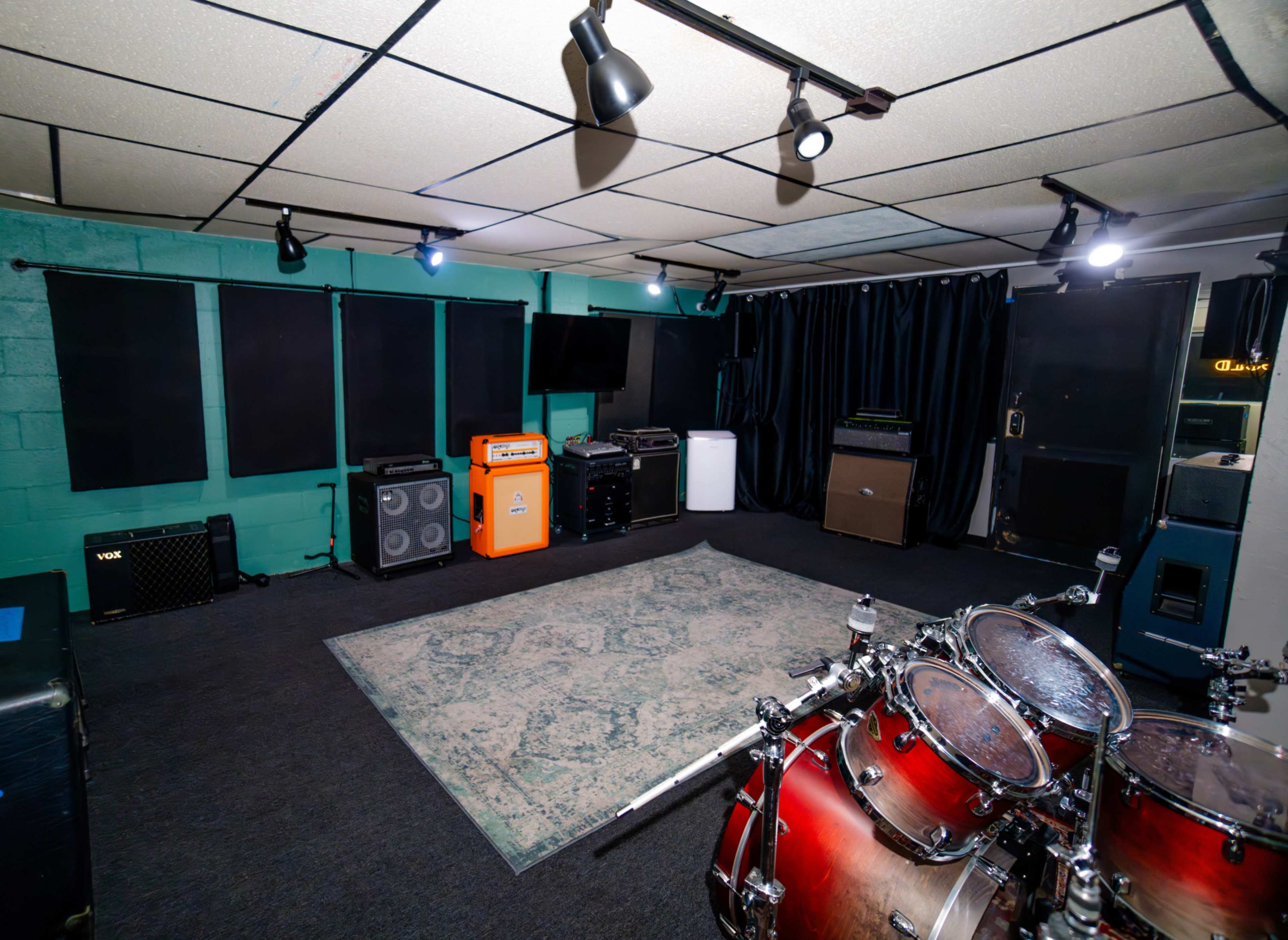 A spacious music rehearsal room with soundproofing, various amplifiers, and a drum set positioned on an area rug.