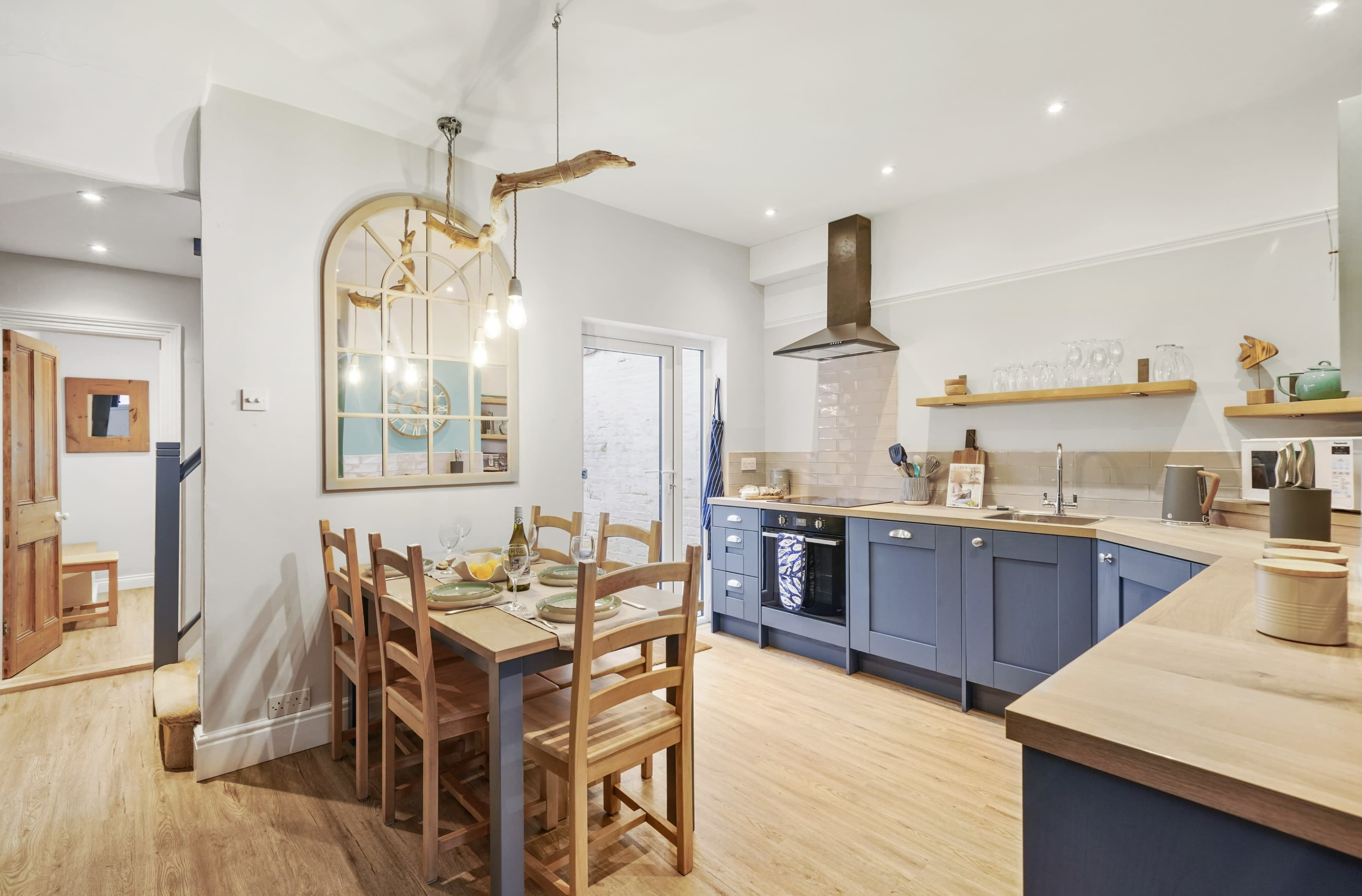 A modern kitchen with blue cabinetry, wooden dining table, and a mix of pendant lighting and natural wood accents.