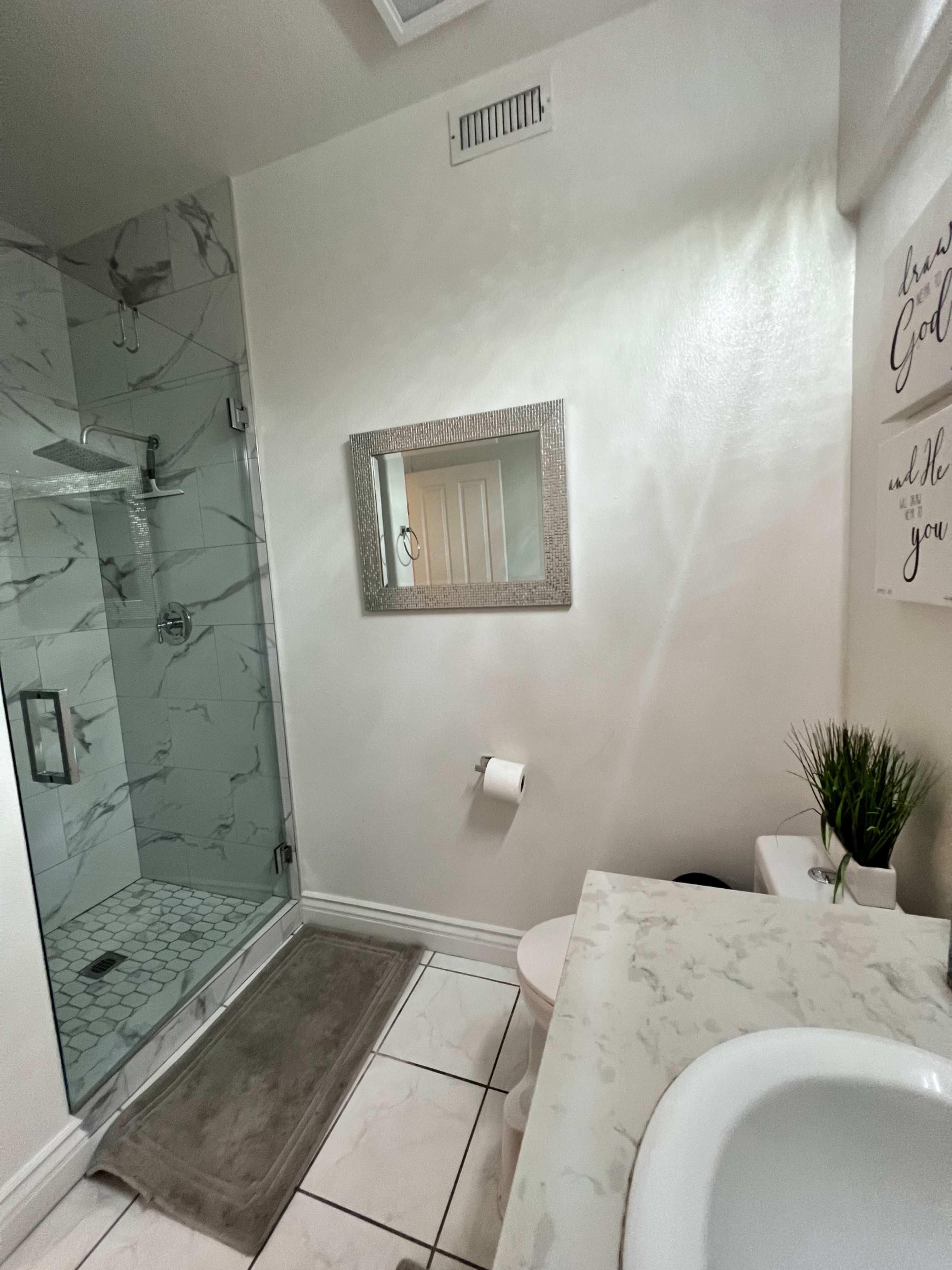 A bathroom with a walk-in shower, a toilet, a sink with a marble countertop, and decorative elements on the walls.
