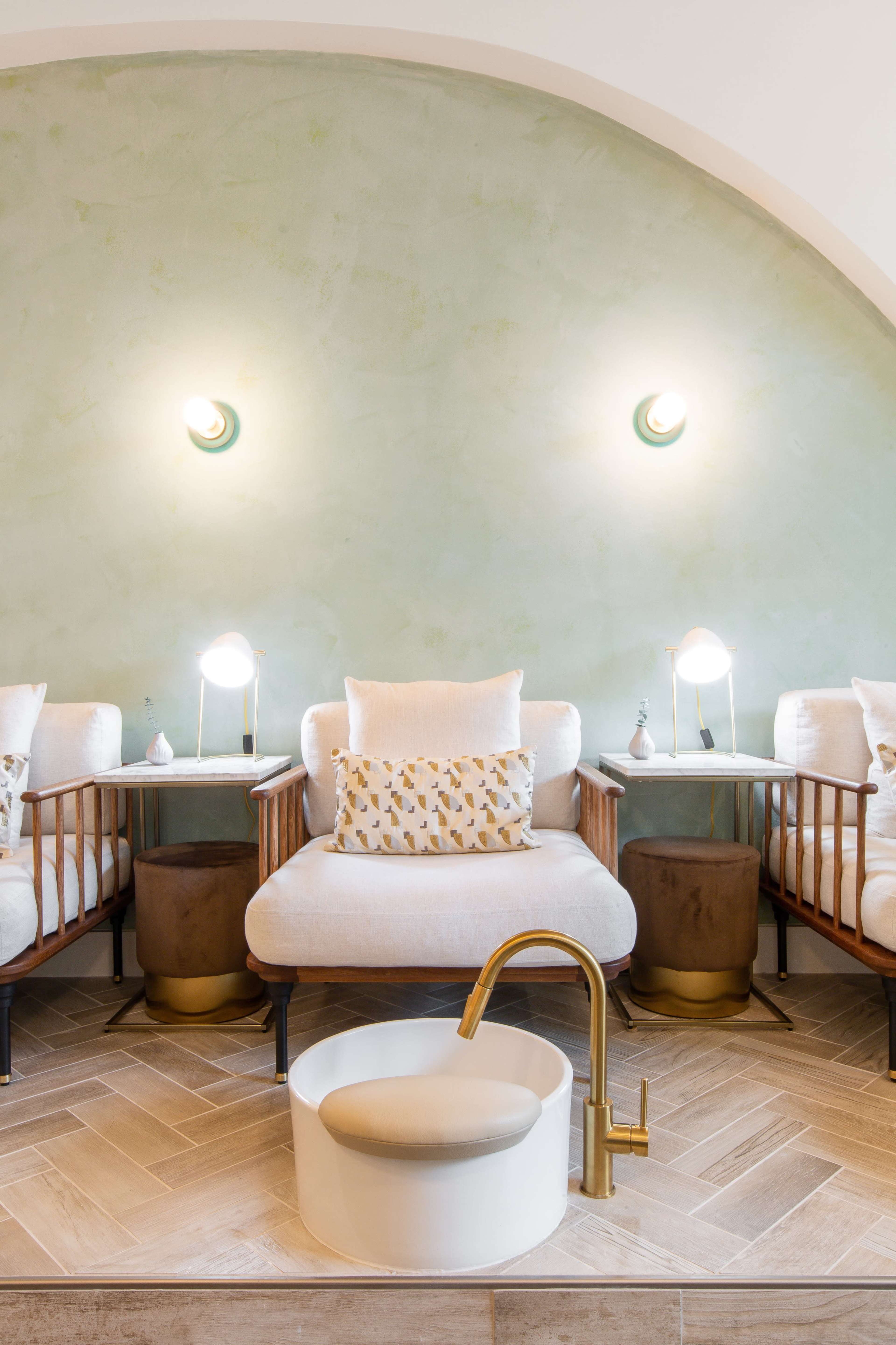 A serene interior space with two armchairs beside small tables and a round basin with a gold faucet in the center.