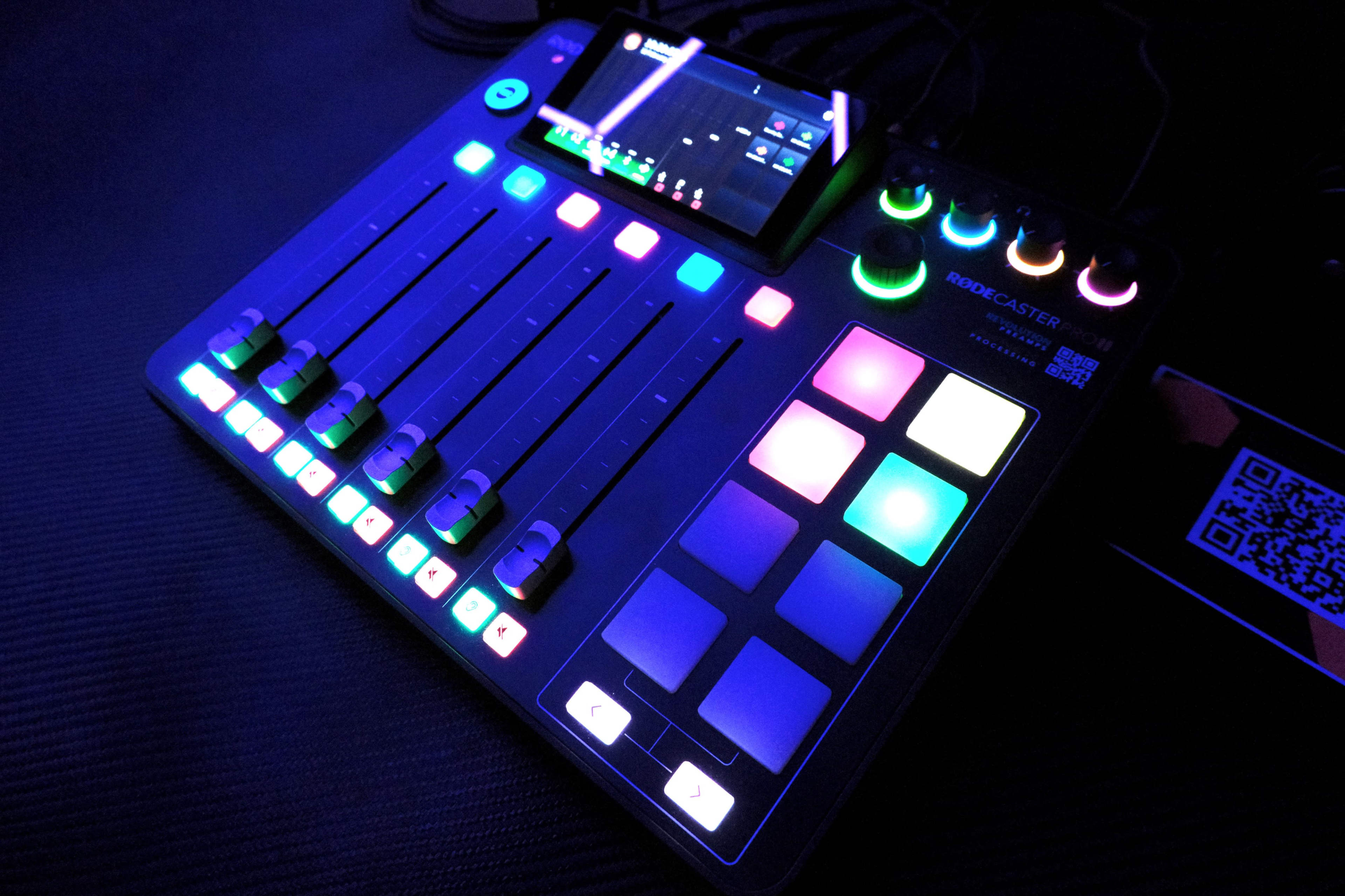 The image shows a colorful audio mixing console with sliders, buttons, and a connected mobile device displaying a digital interface.