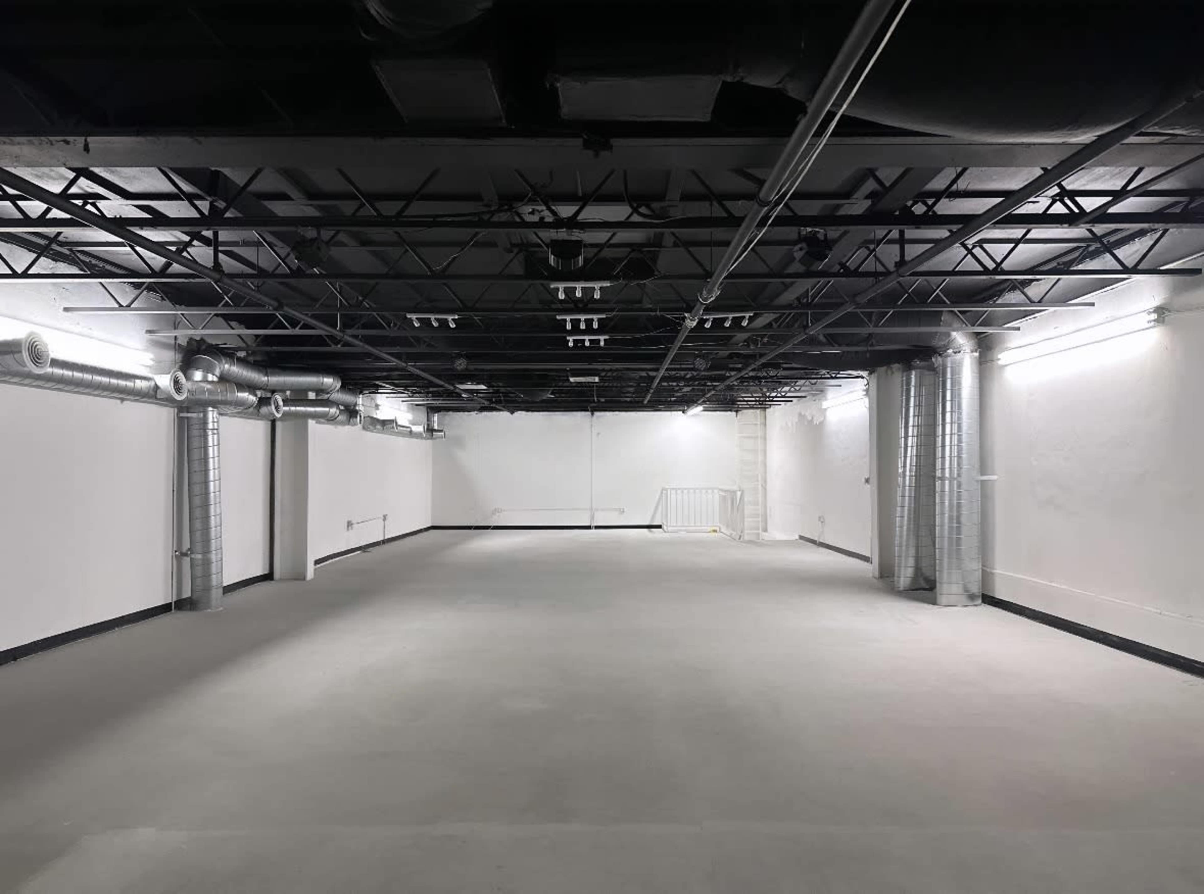 A spacious, empty basement with exposed ductwork and overhead lighting.