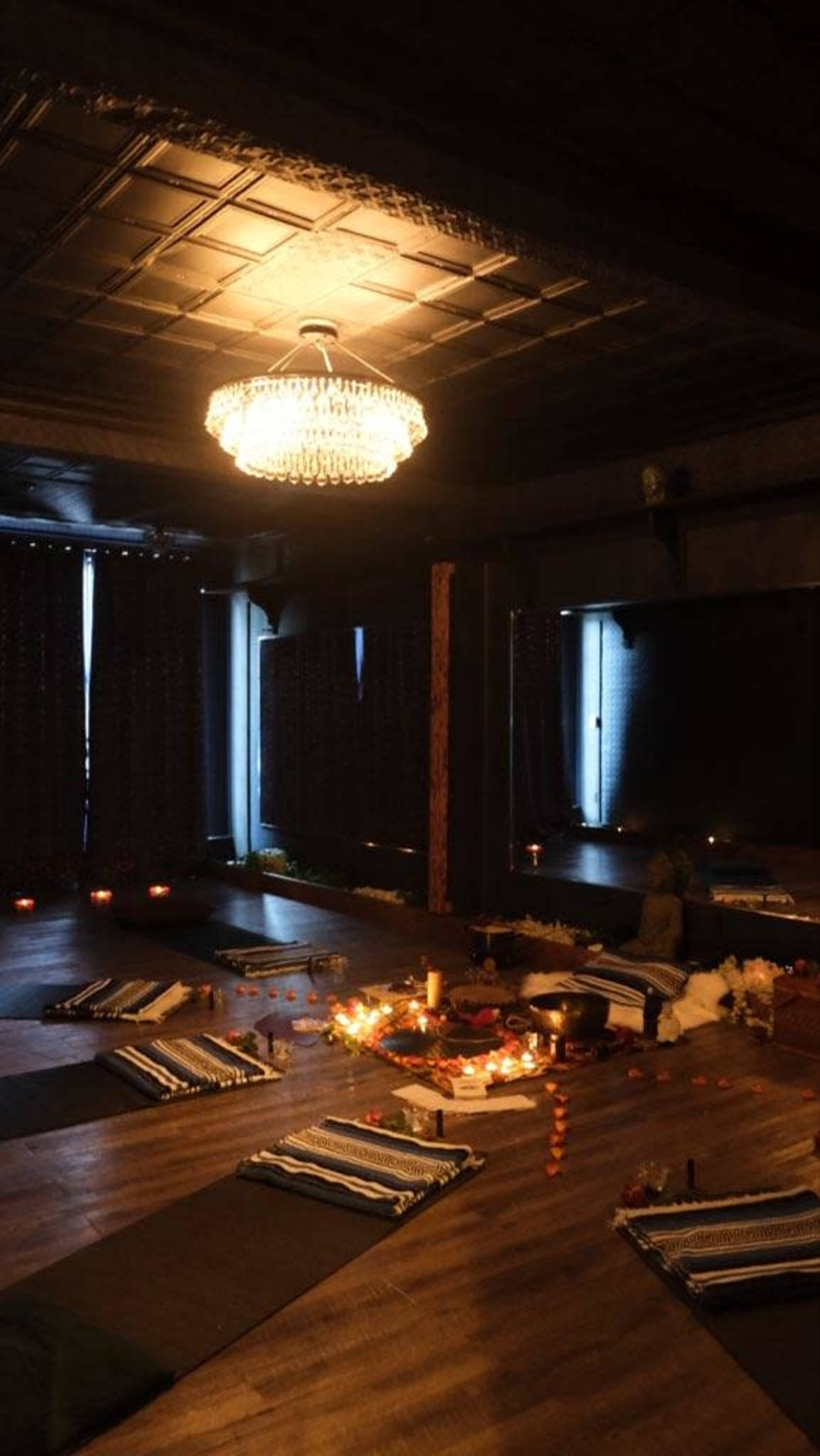 The room features a low-lit setting with meditation mats arranged on a wooden floor, surrounded by candles and an altar adorned with various offerings.