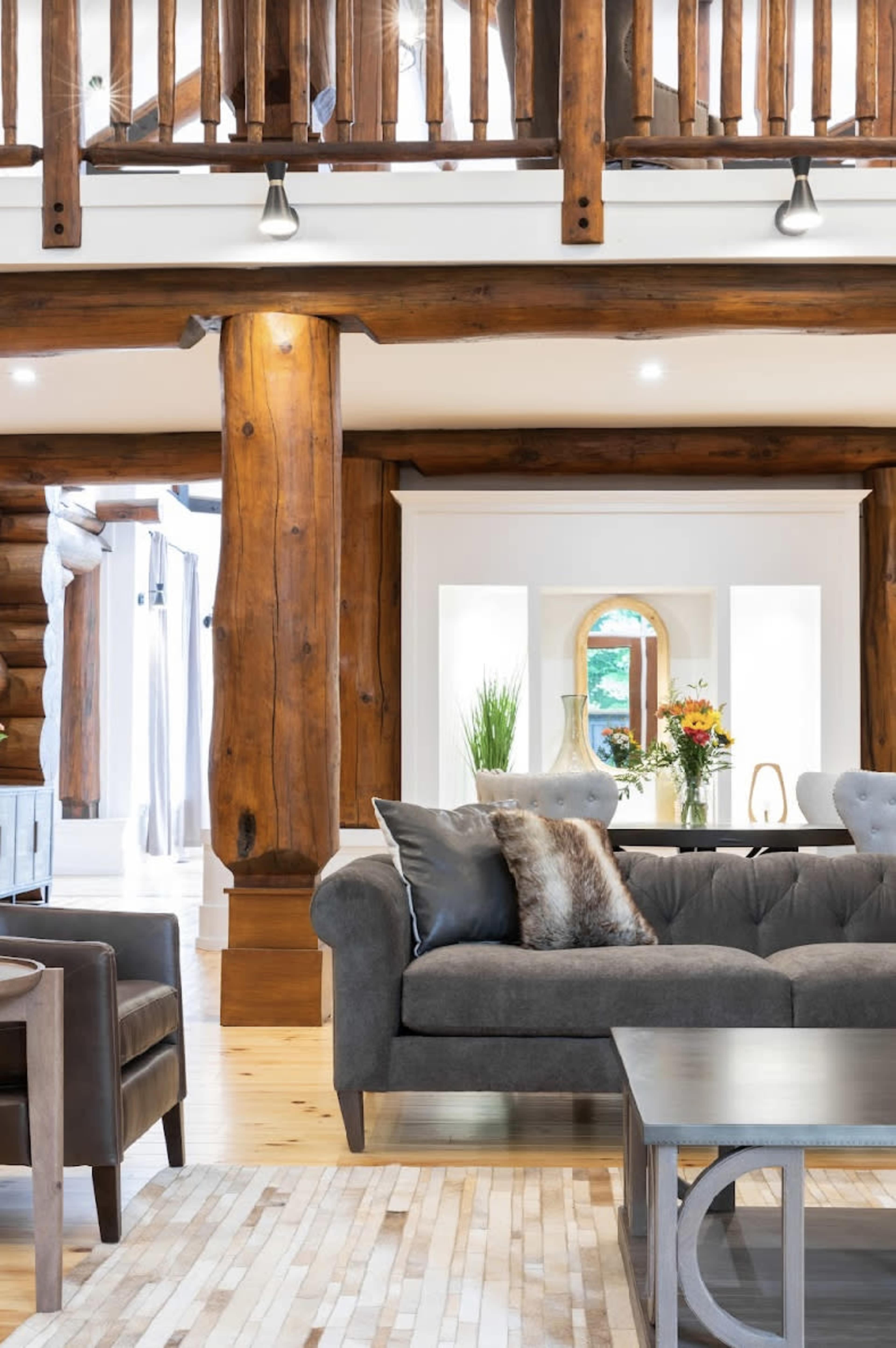 A cozy living room with wooden beams, a gray sofa, and a coffee table, featuring a vase of flowers and a bright, airy atmosphere.